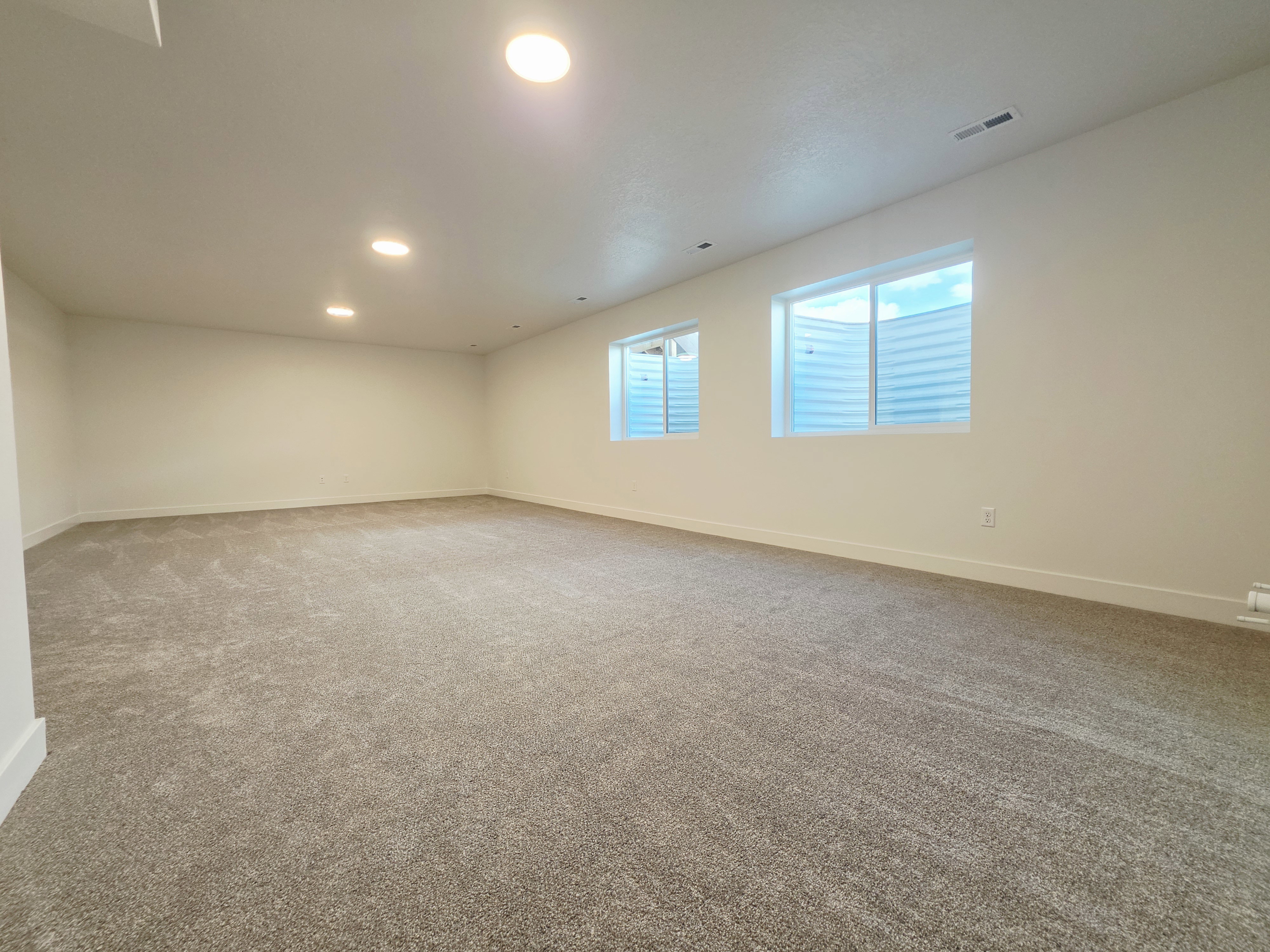 Expansive room featuring plush carpet flooring, recessed lighting, and a neutral color palette