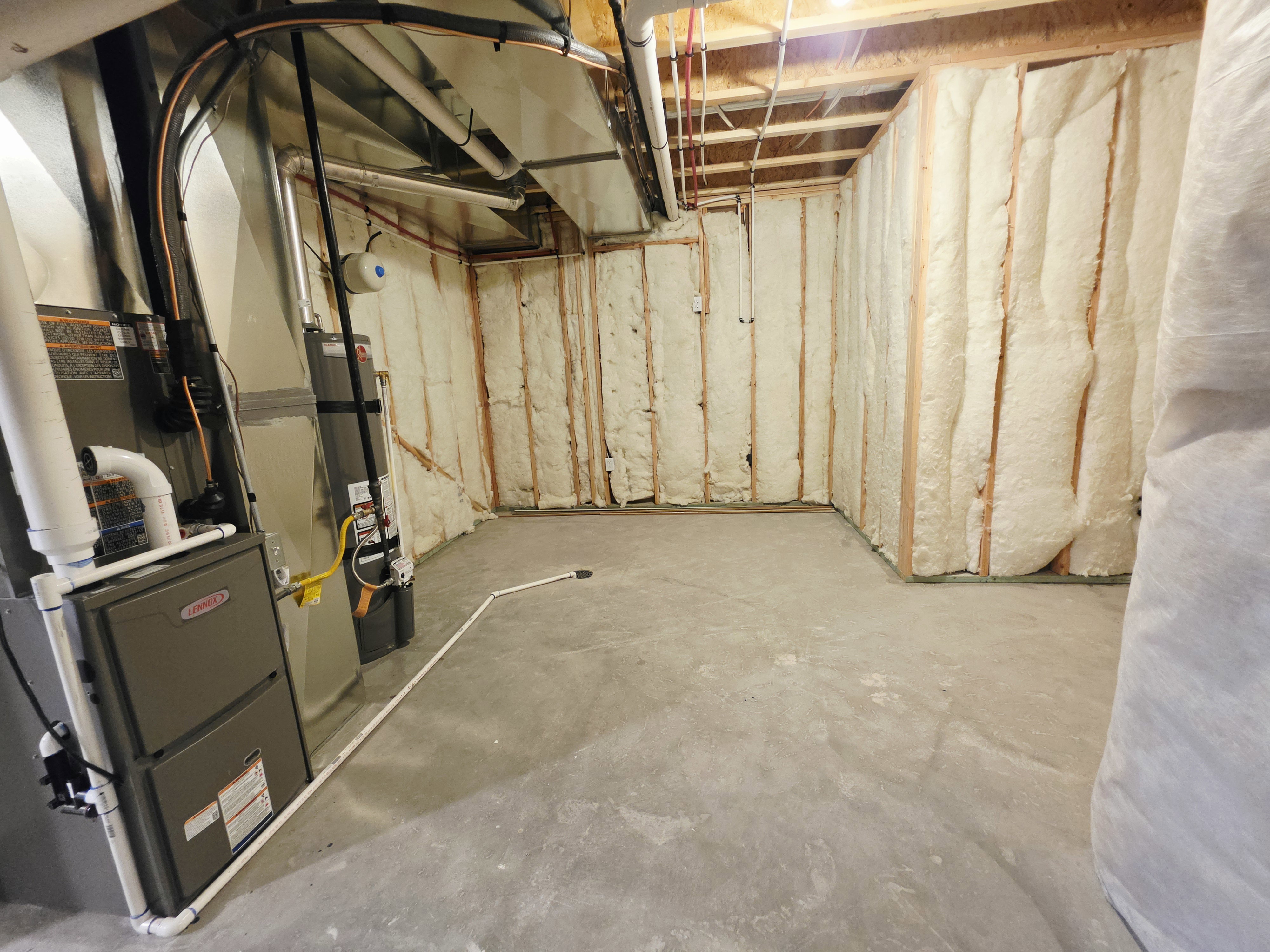 Unfinished basement space featuring spray foam insulation, exposed wood framing, concrete flooring, and visible HVAC systems