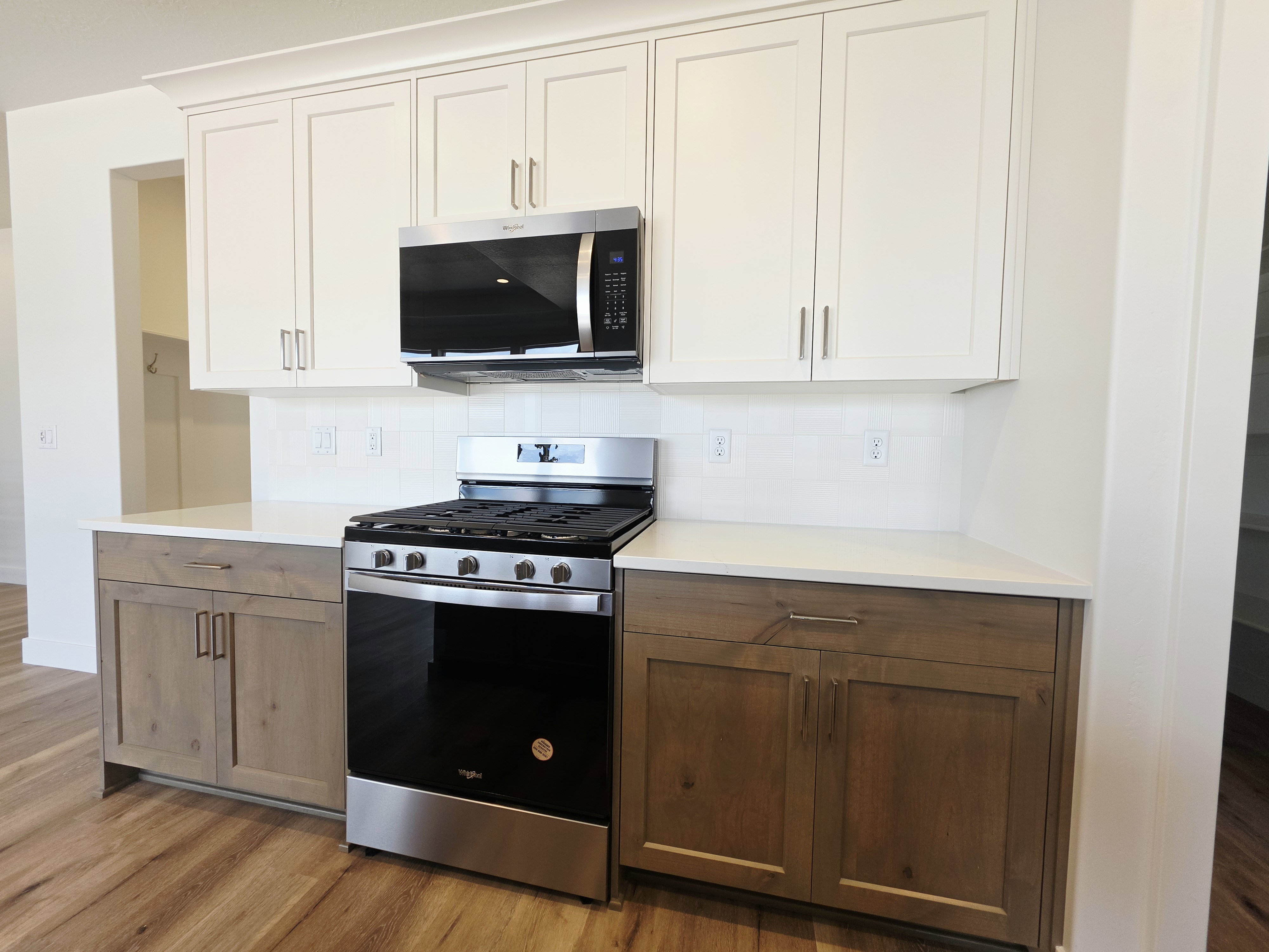 Kitchen featuring a stainless steel Whirlpool range with an overhead microwave, white upper cabinetry, wood-finish lower cabinetry, white countertops, and a white subway tile backsplash