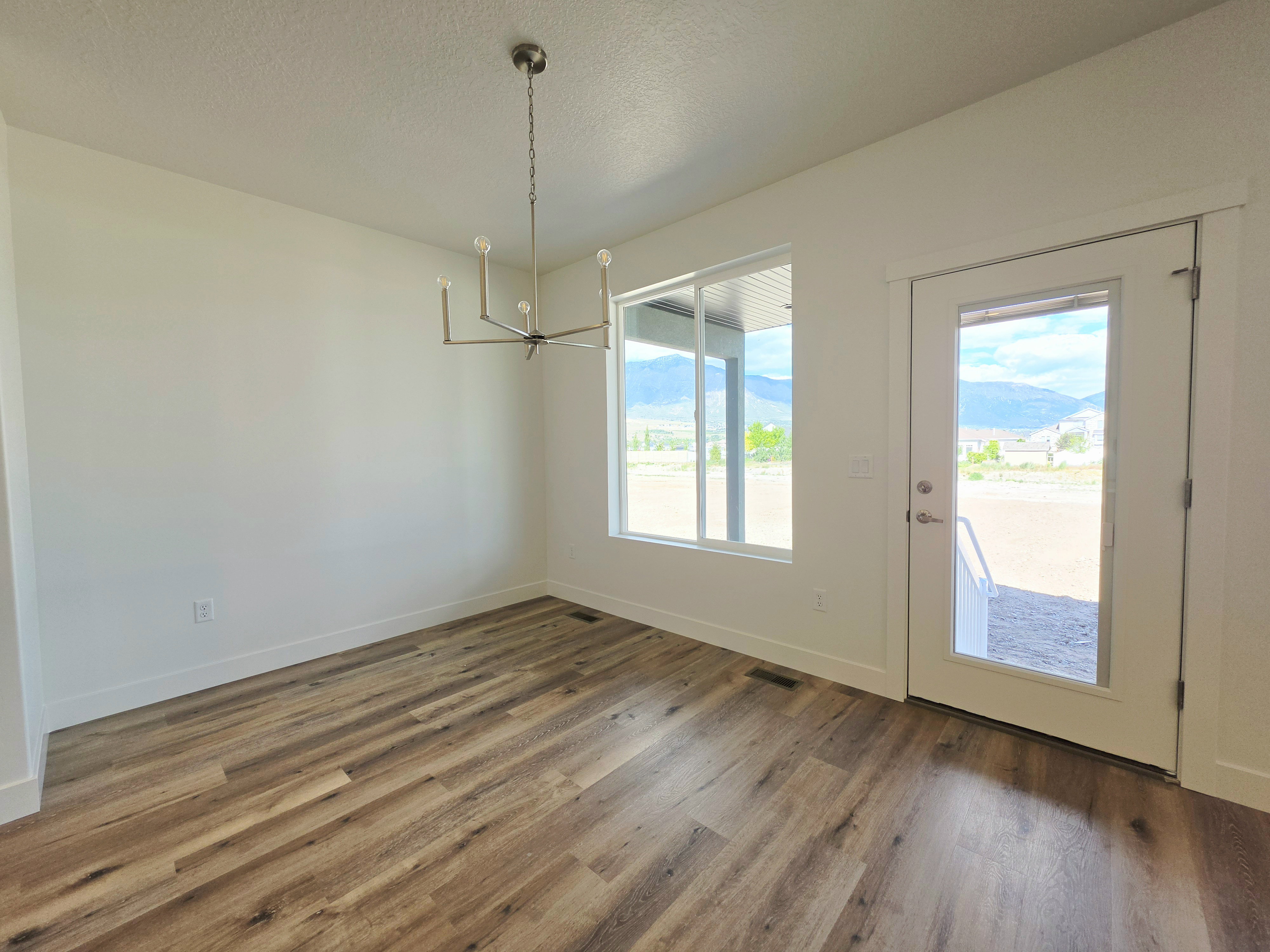 Spacious room featuring wood-finish flooring, a contemporary chandelier, large windows, white baseboards, and a glass-paneled exterior door