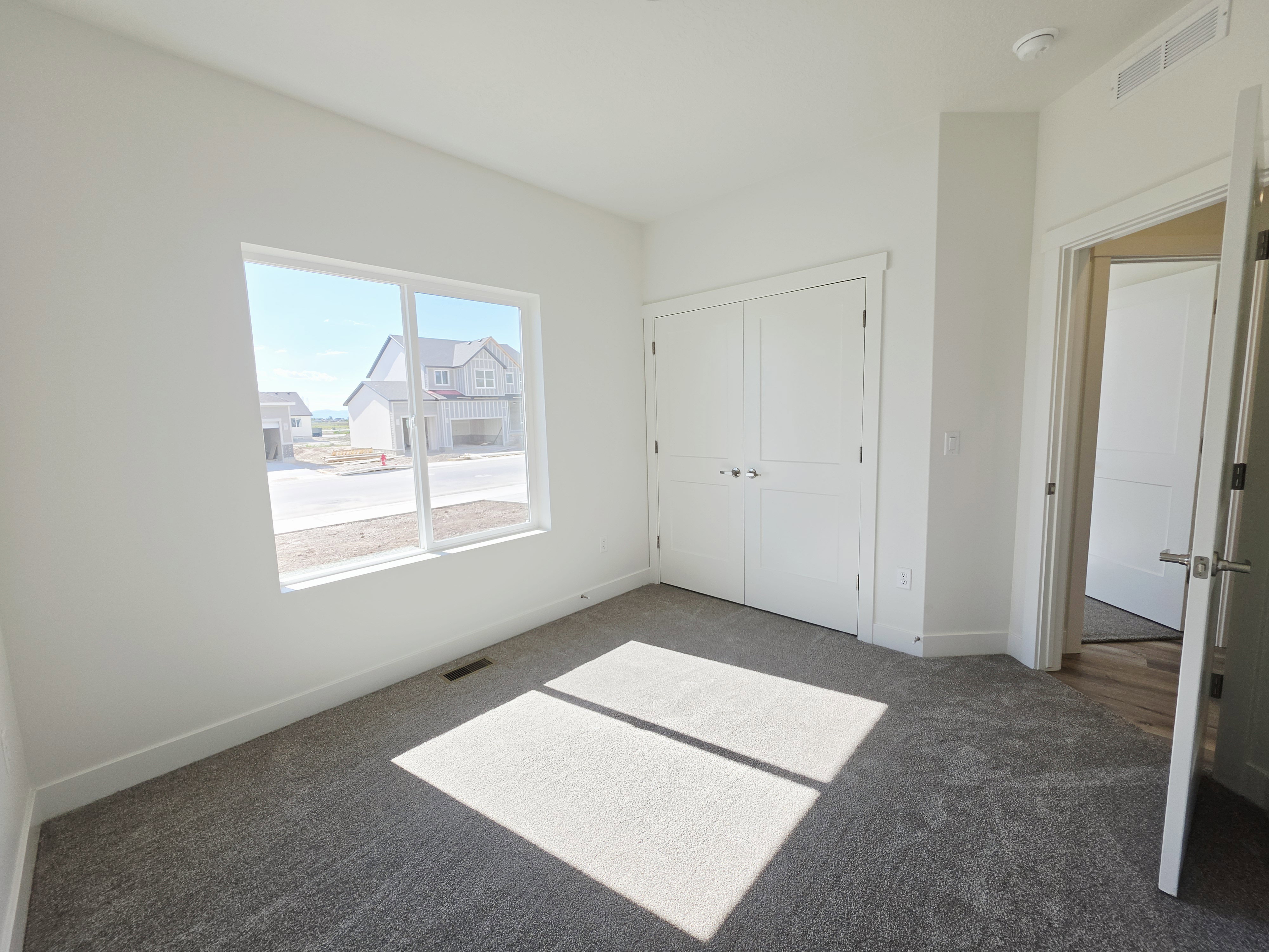 Bright interior space featuring a large window, neutral carpeting, white trim, a closet with double bi-fold doors, and a solid core door with a polished chrome handle
