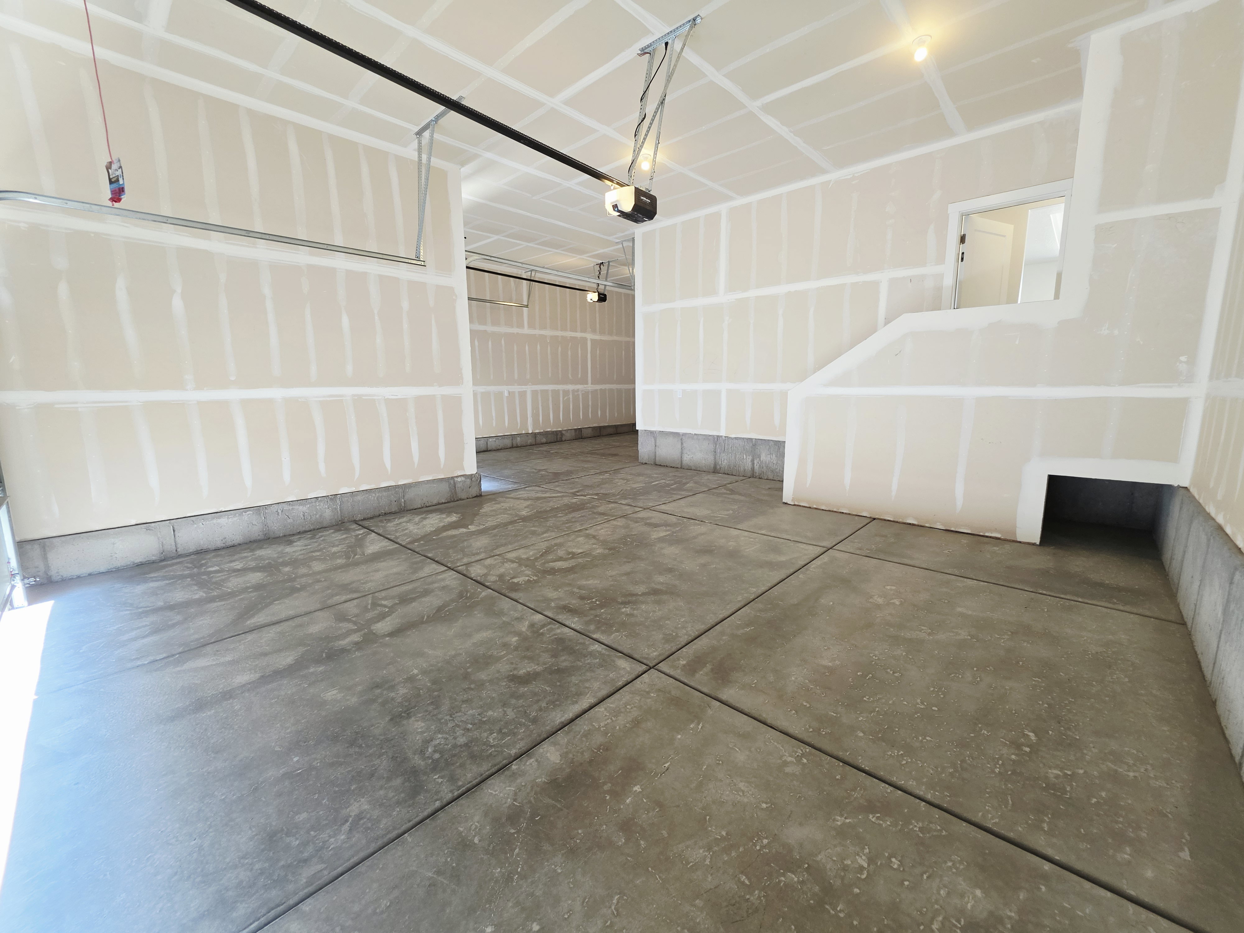 Spacious garage with unfinished drywall, concrete flooring, exposed ceiling joists, and integrated garage door opener