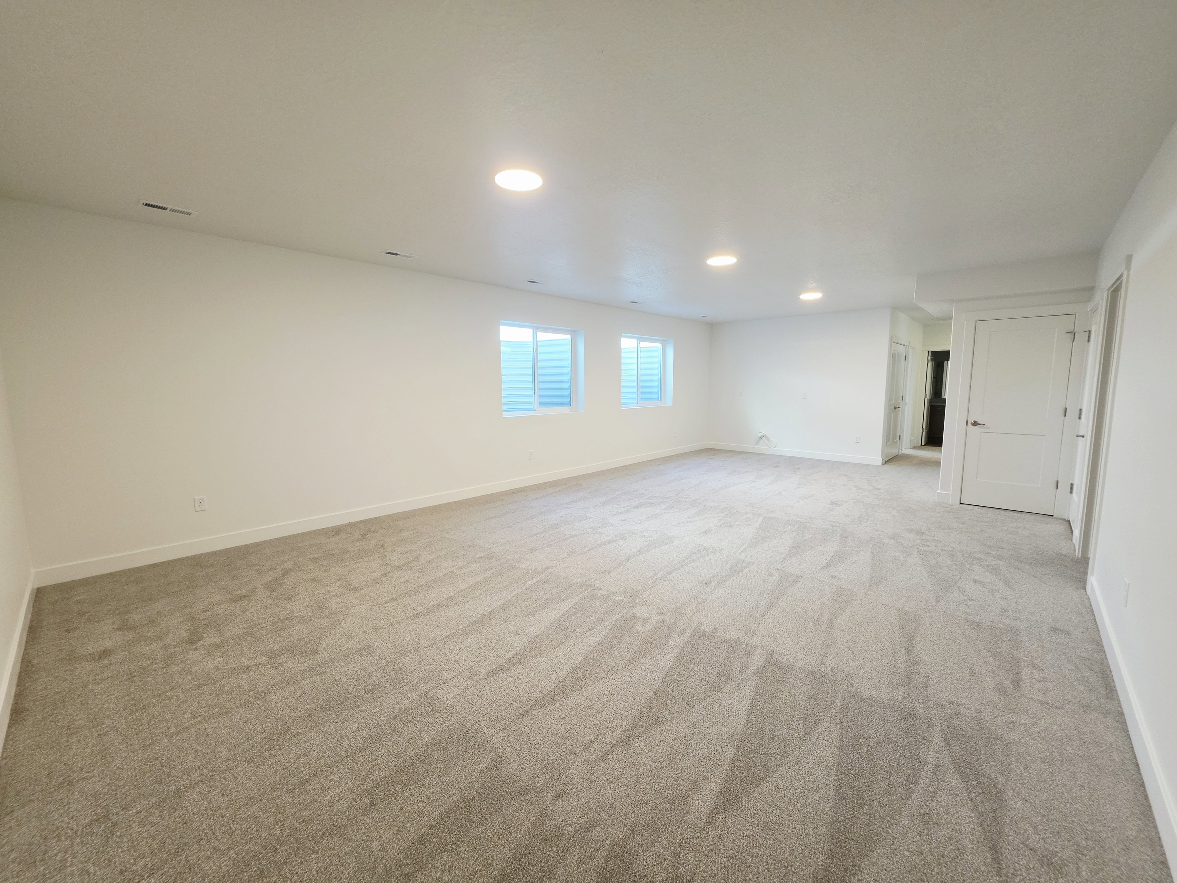 Spacious room featuring neutral carpeting, recessed lighting, and white baseboards