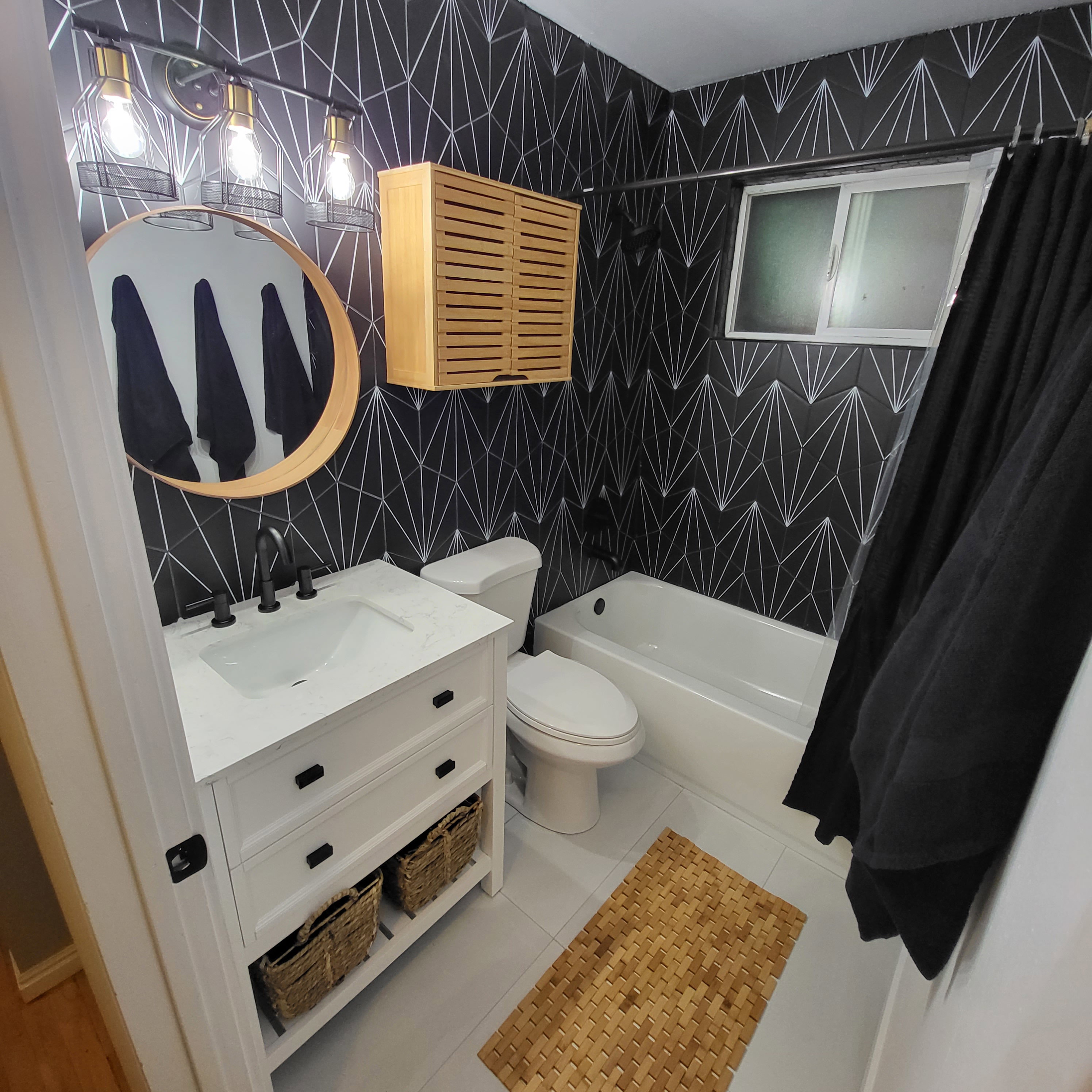 Bathroom featuring a white vanity with black hardware, a circular mirror, and a wall-mounted light fixture