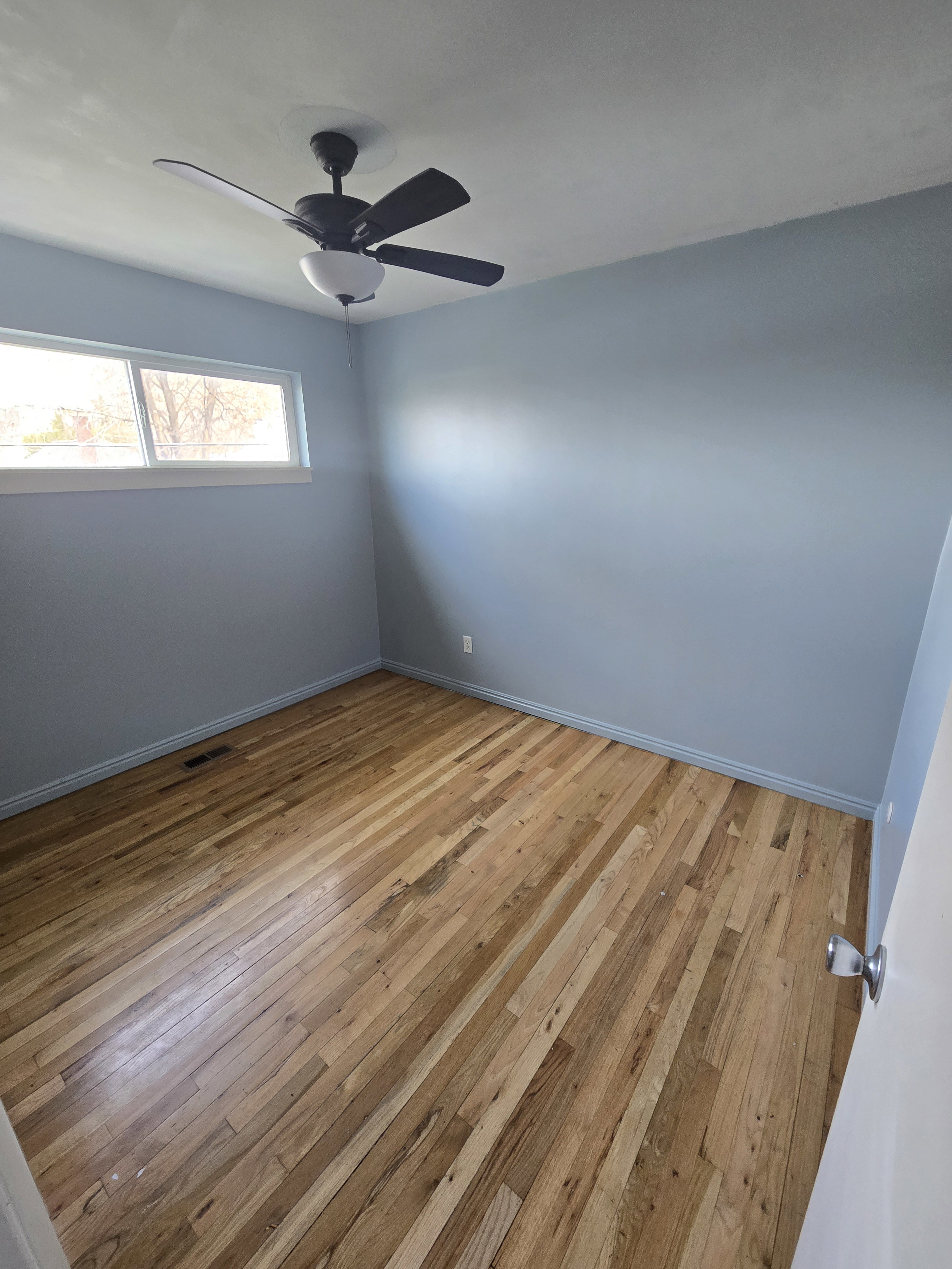 Hardwood flooring with a natural finish, light blue walls, and a ceiling fan with integrated lighting