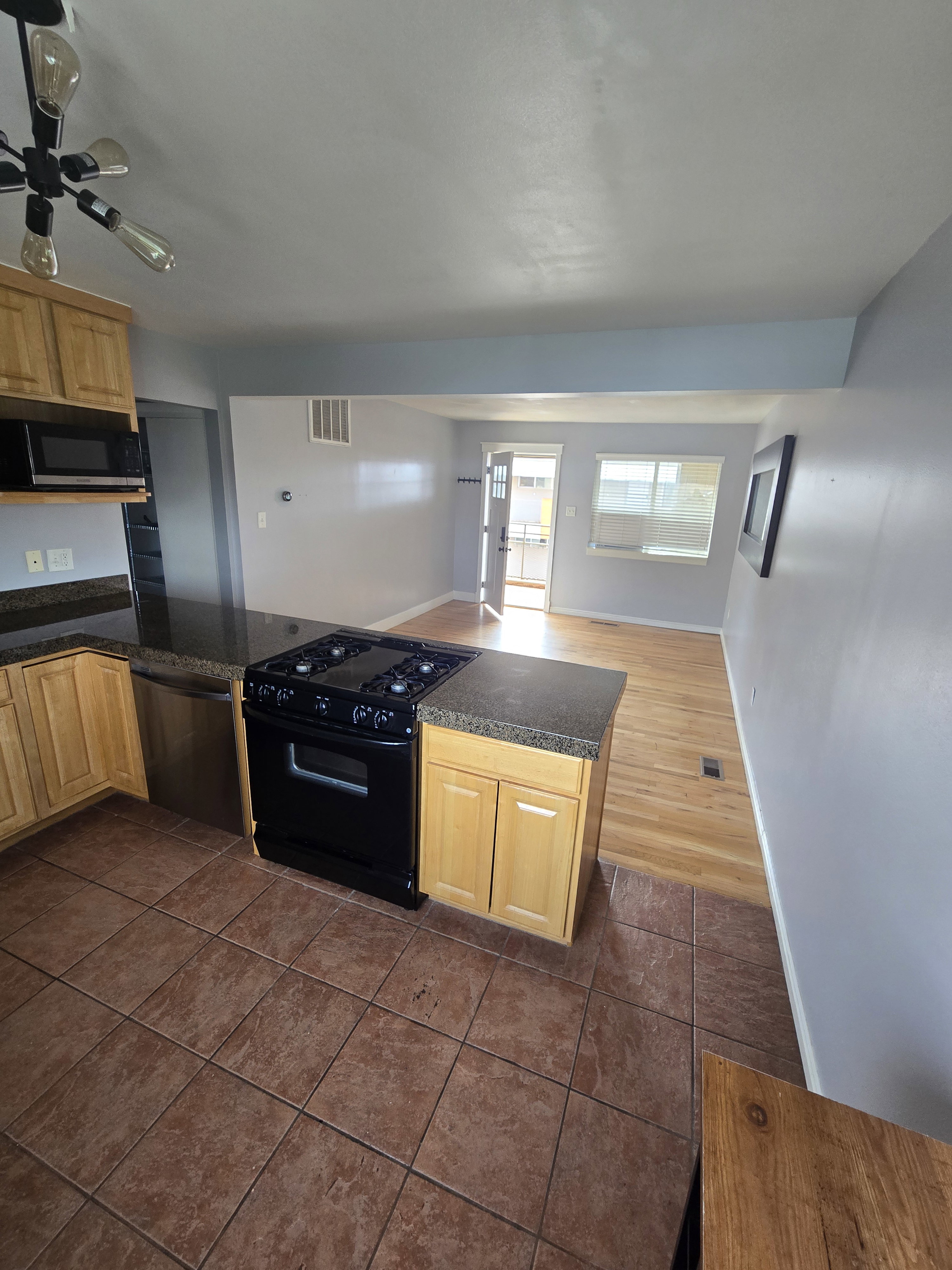 Kitchen featuring wood cabinetry, dark countertops, a built-in black gas range, a stainless steel dishwasher, and ceramic tile flooring