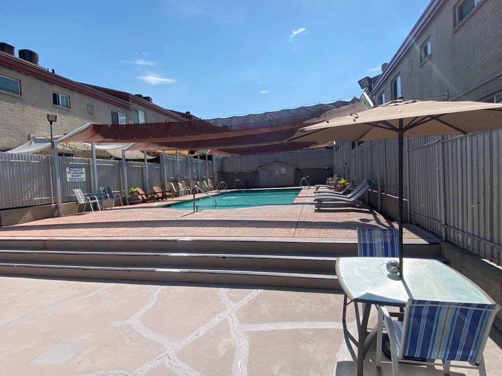 Outdoor swimming pool area with concrete decking, perimeter fencing, and shade structures