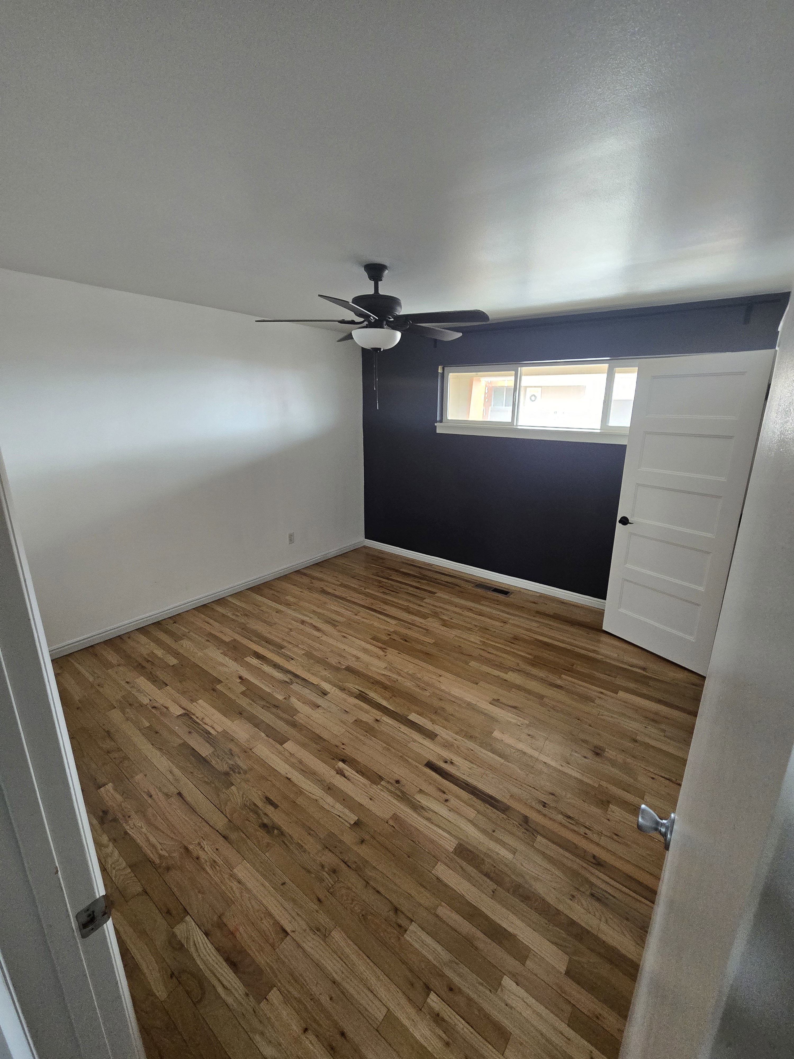 Spacious room featuring wood-finish flooring, a contemporary ceiling fan with integrated lighting, and a multi-pane window