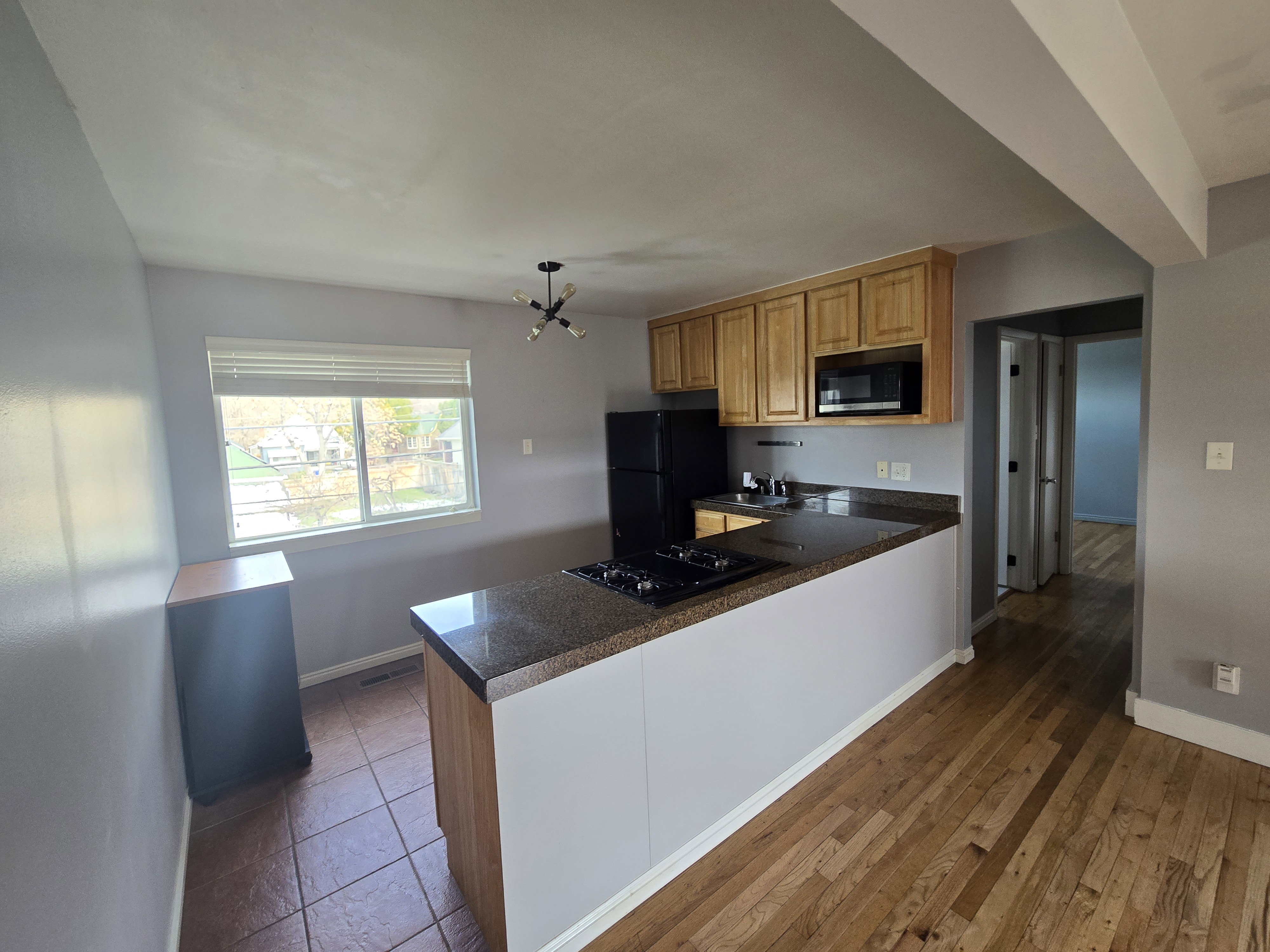 Kitchen area featuring wood cabinetry, black appliances, a built-in cooktop, and a granite-finish countertop