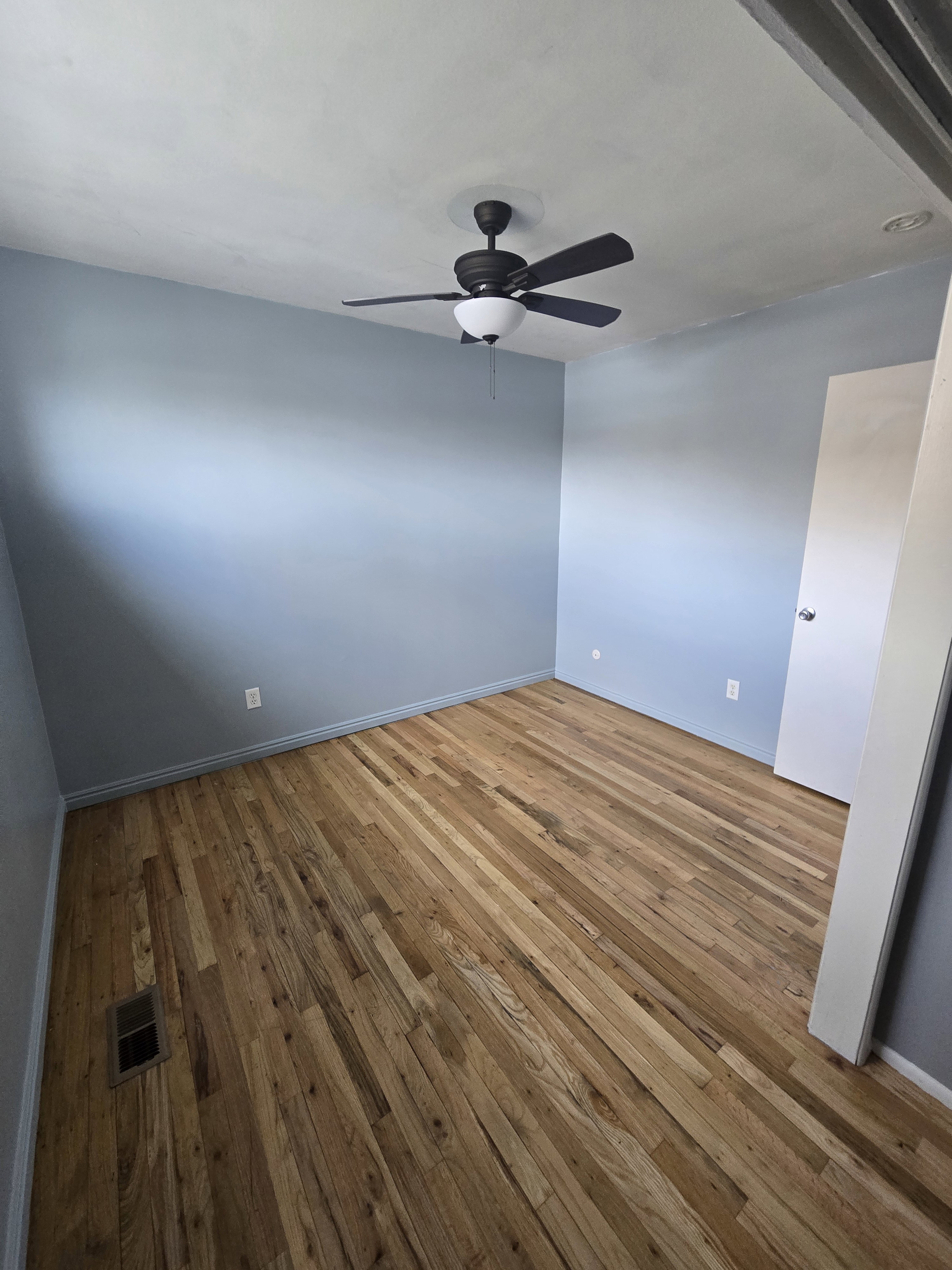 Room featuring wood-finish flooring, light blue painted walls, and a ceiling fan with integrated lighting