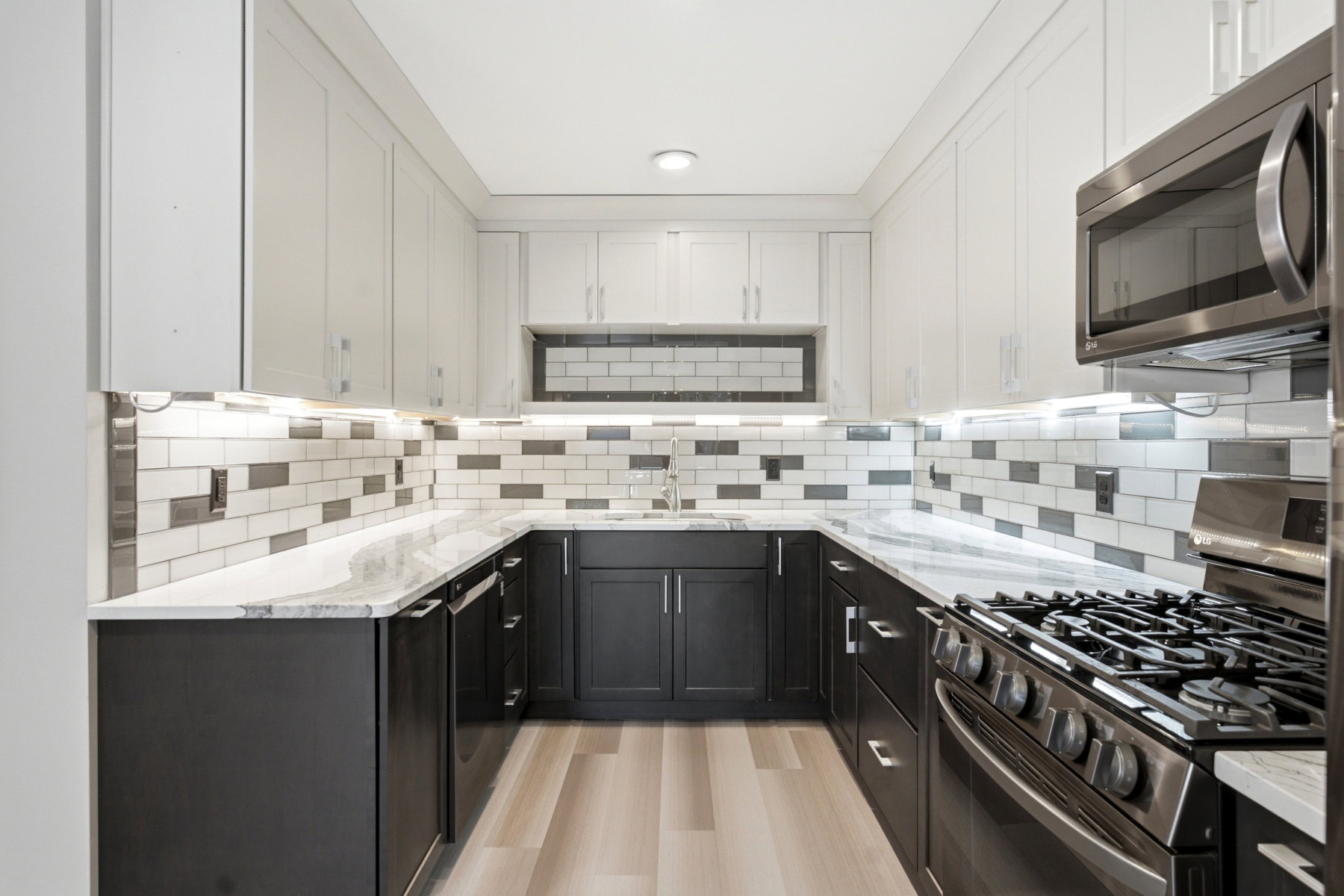 U-shaped kitchen featuring white upper cabinetry, dark lower cabinetry, light countertops, and a patterned subway tile backsplash