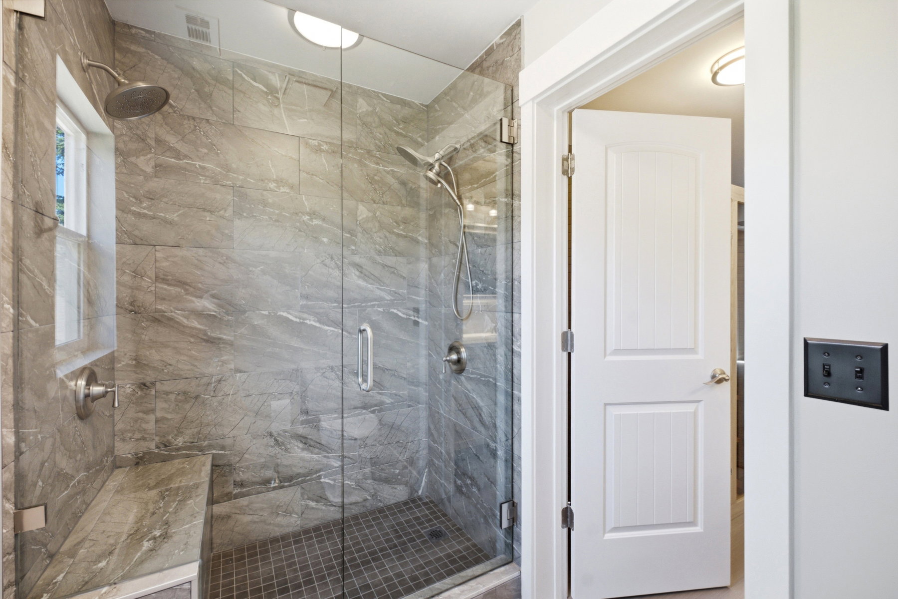 Walk-in shower with full-height stone-look tile, glass enclosure, and built-in bench