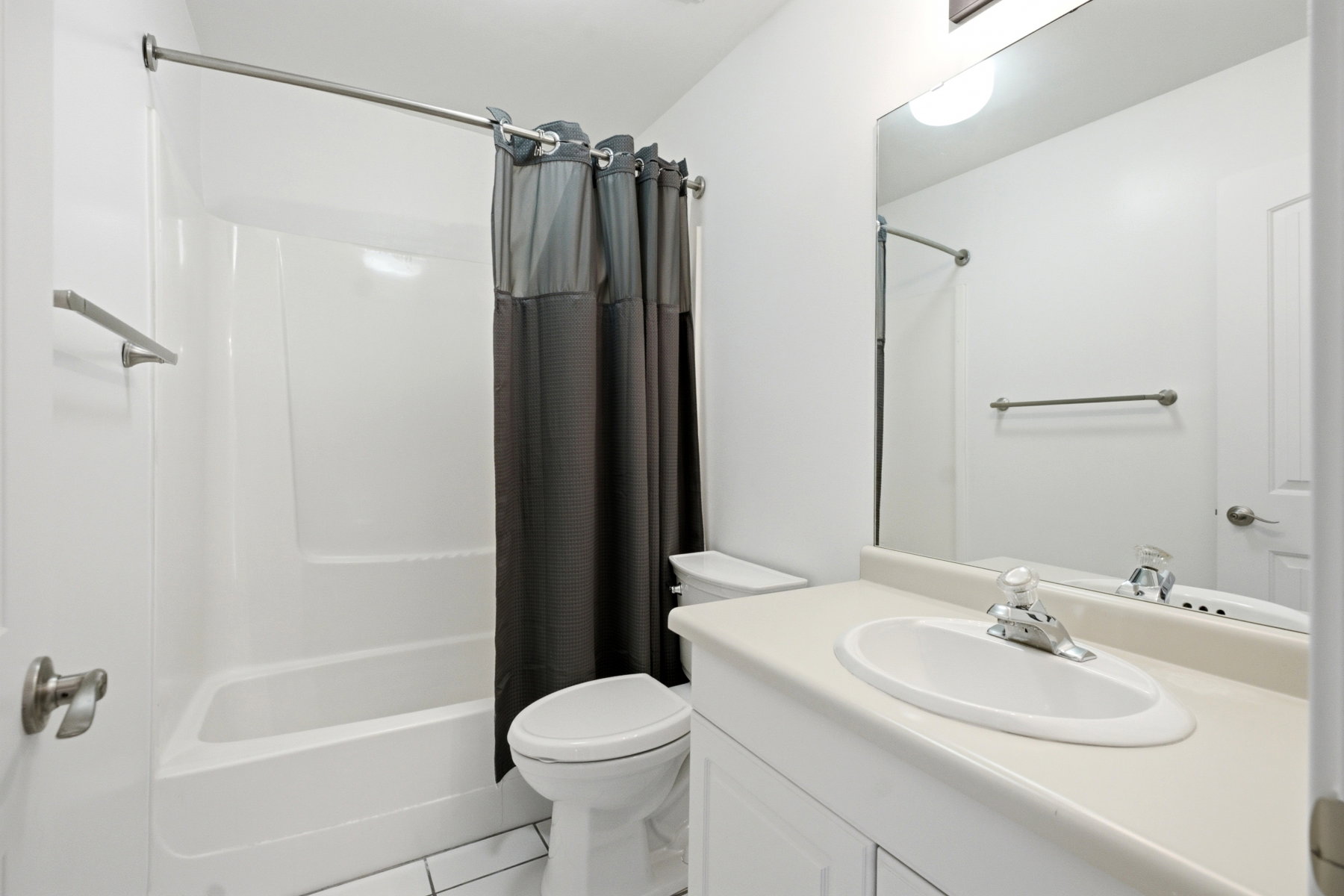 Bathroom featuring an integrated shower/tub combination, a vanity with an integrated sink, a large wall-mounted mirror, and white tile flooring