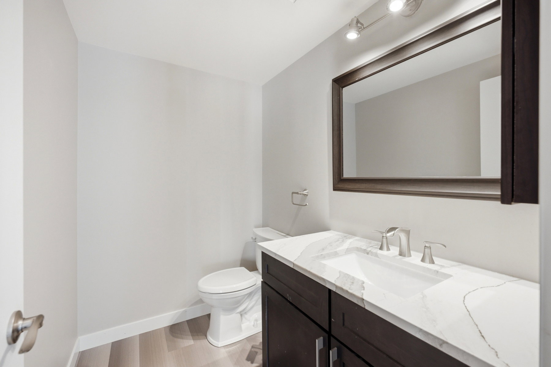 Bathroom featuring a dark wood-finish vanity with a light countertop, an integrated rectangular sink, and a framed mirror