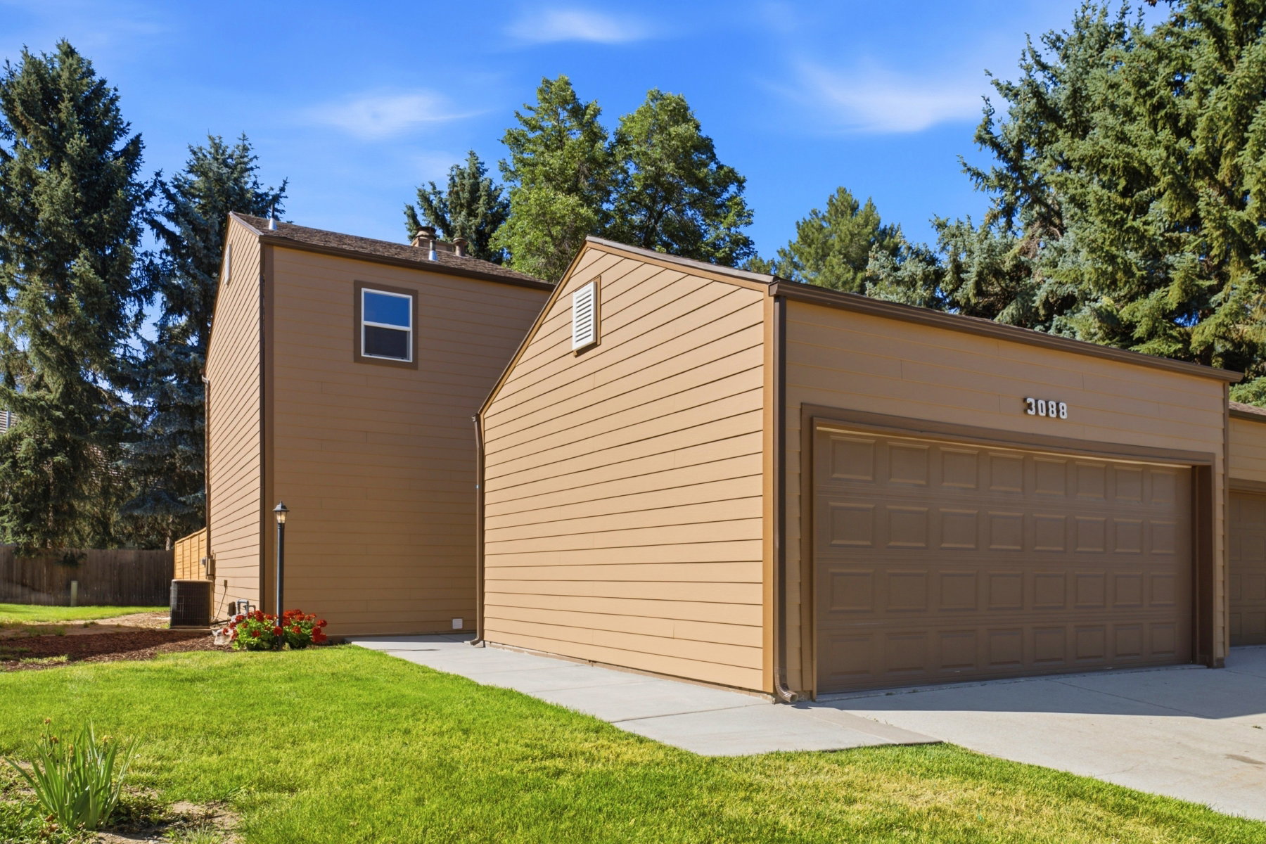 Two-story residence featuring a two-car garage with an overhead panel door, a concrete driveway, and mature perimeter trees