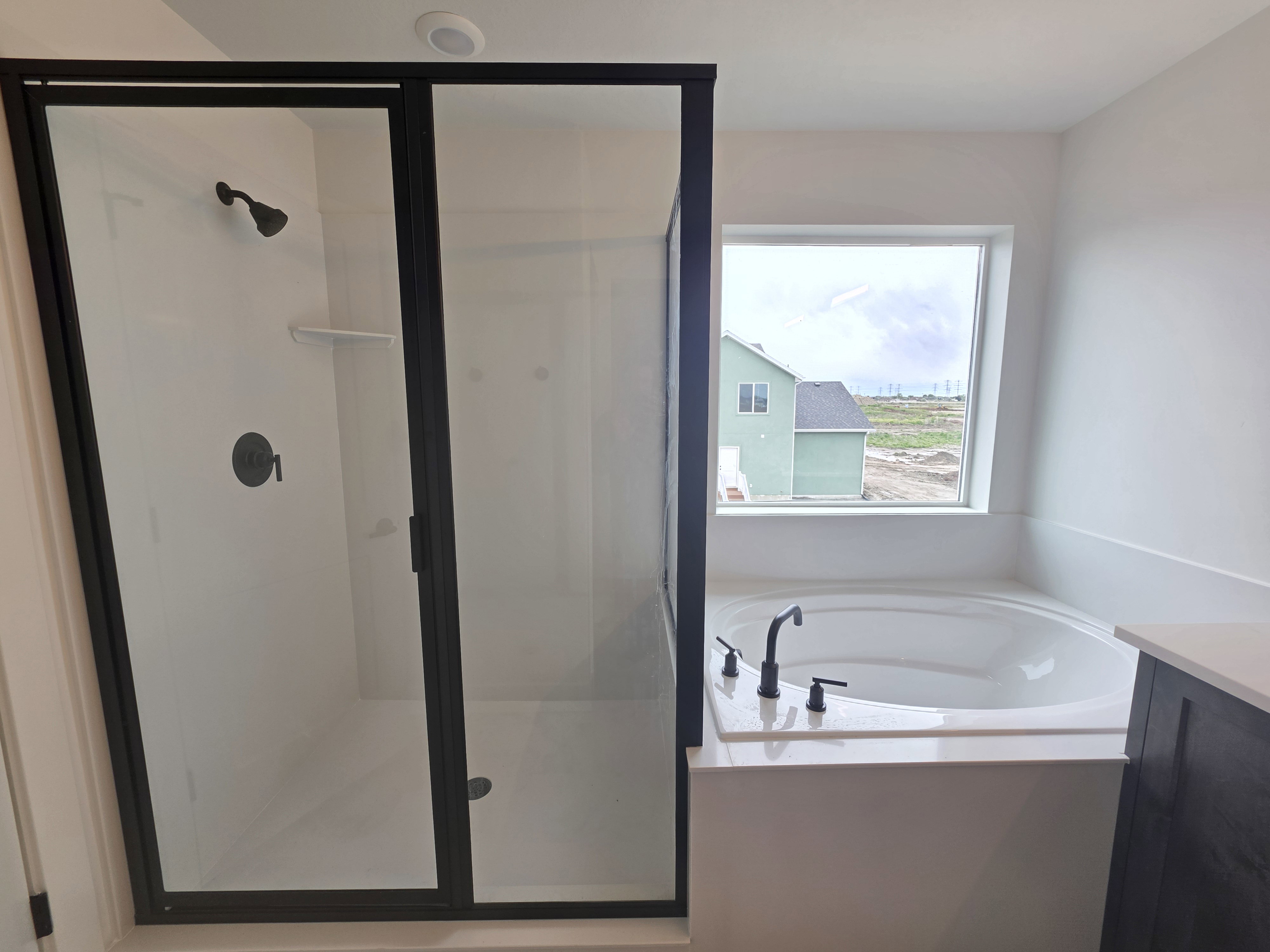 Modern bathroom featuring a walk-in shower with matte black framing and fixtures, a built-in shelf, and a large soaking tub with coordinating matte black fixtures set beneath a window