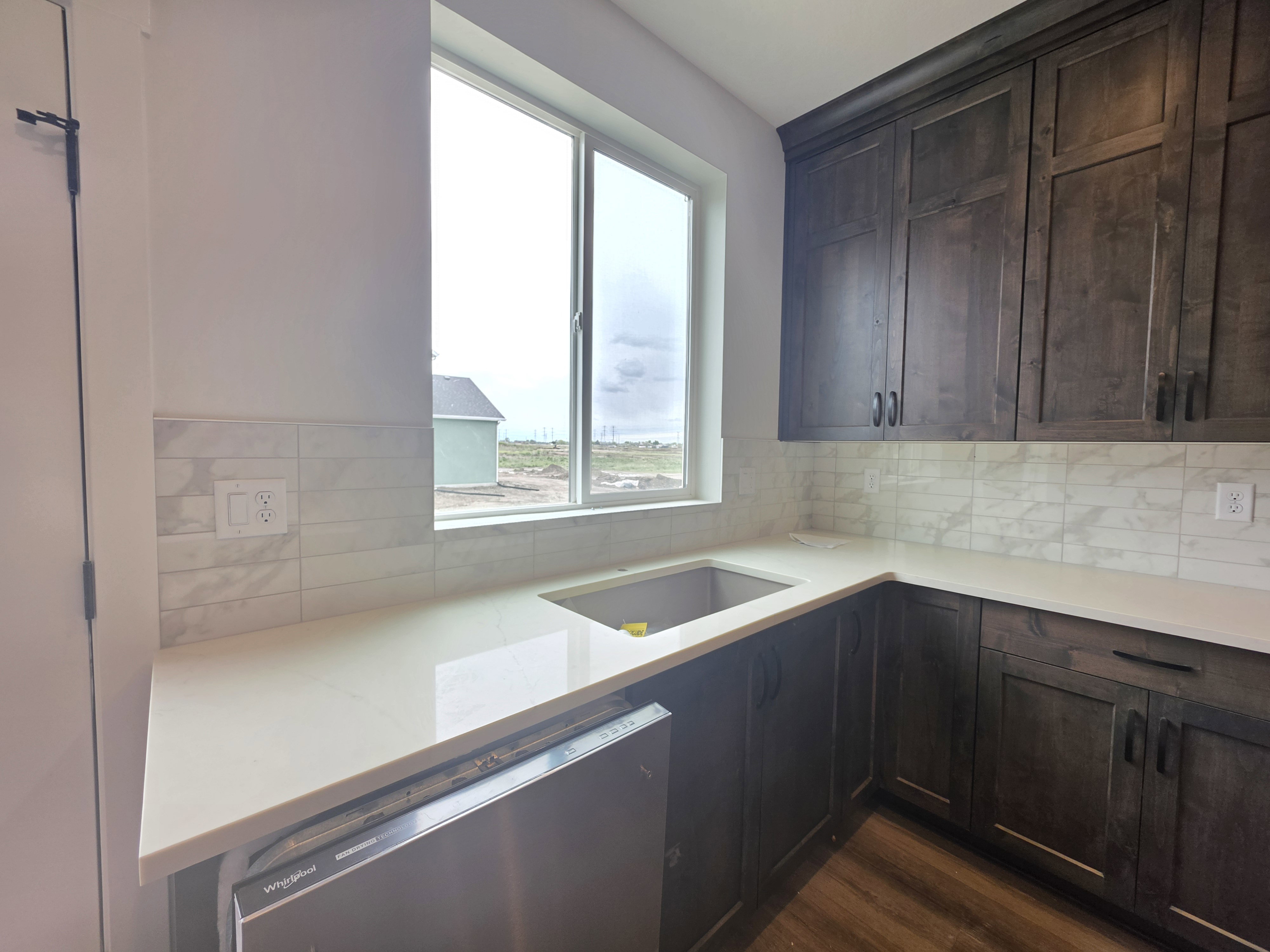 Kitchen featuring dark wood cabinetry, light-toned countertops, and a white tile backsplash