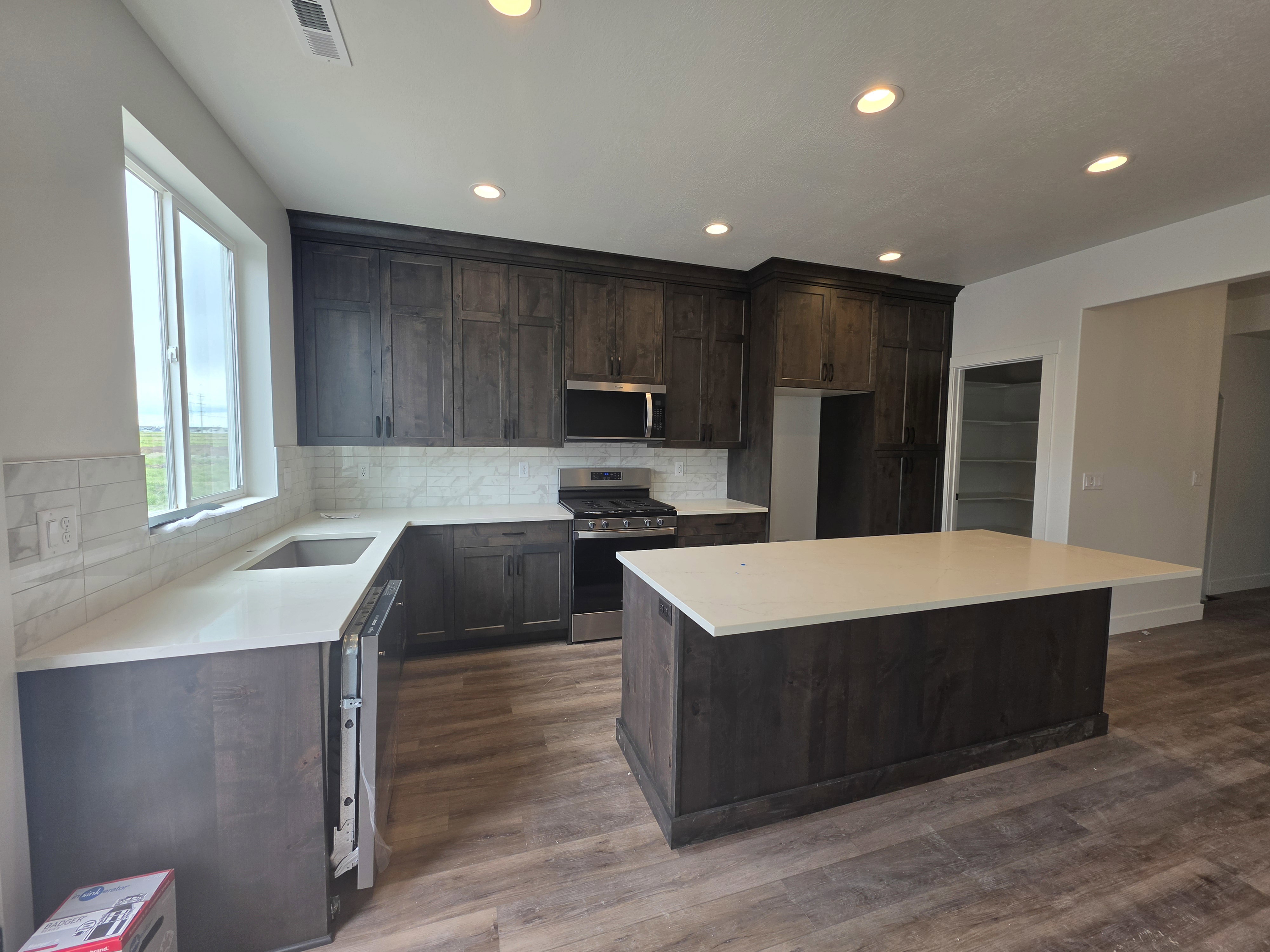 Open-concept kitchen featuring dark wood-finish cabinetry, light countertops, and wood-finish flooring