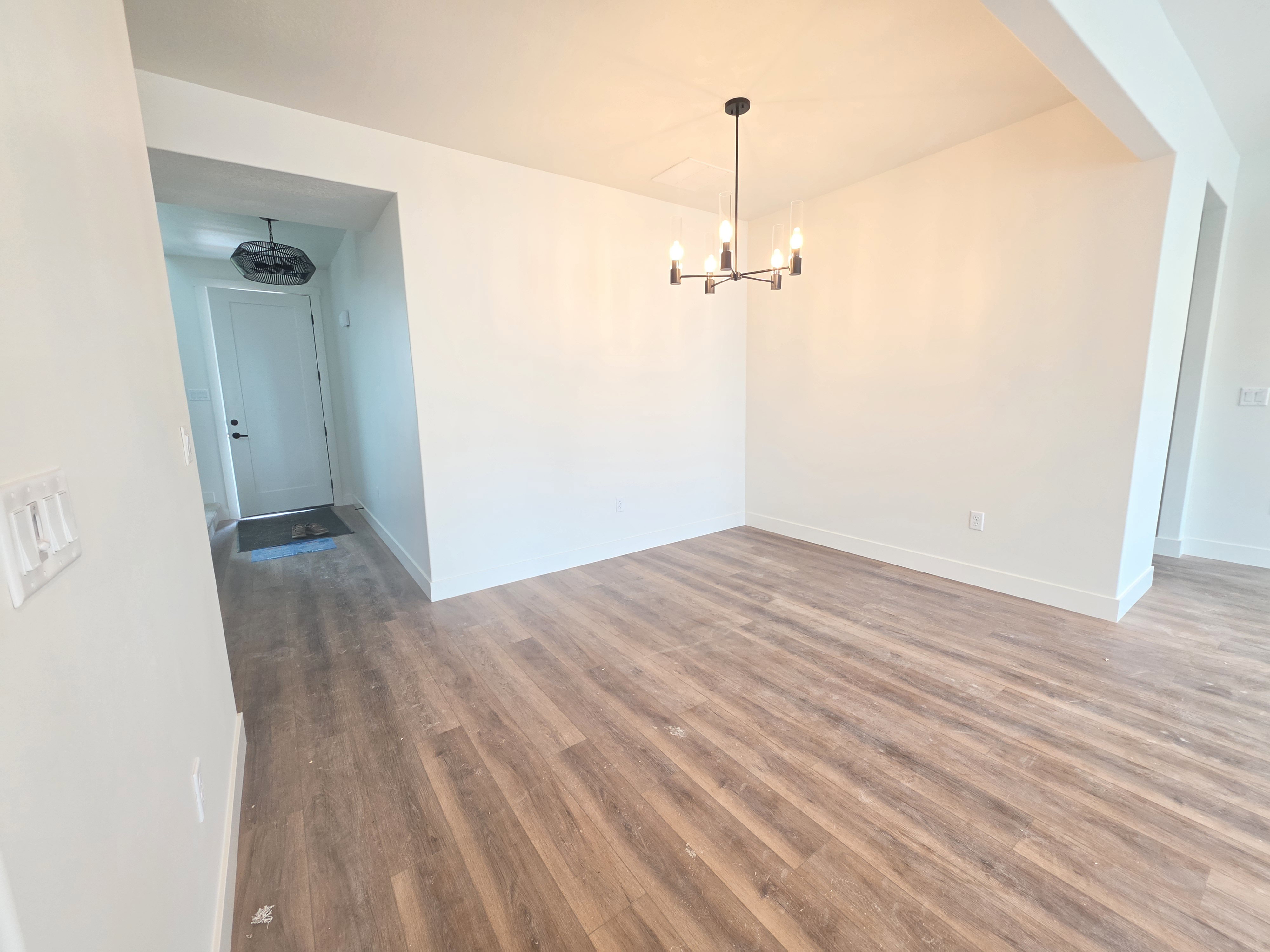 Open concept space featuring wood-finish flooring, white walls, and a contemporary chandelier