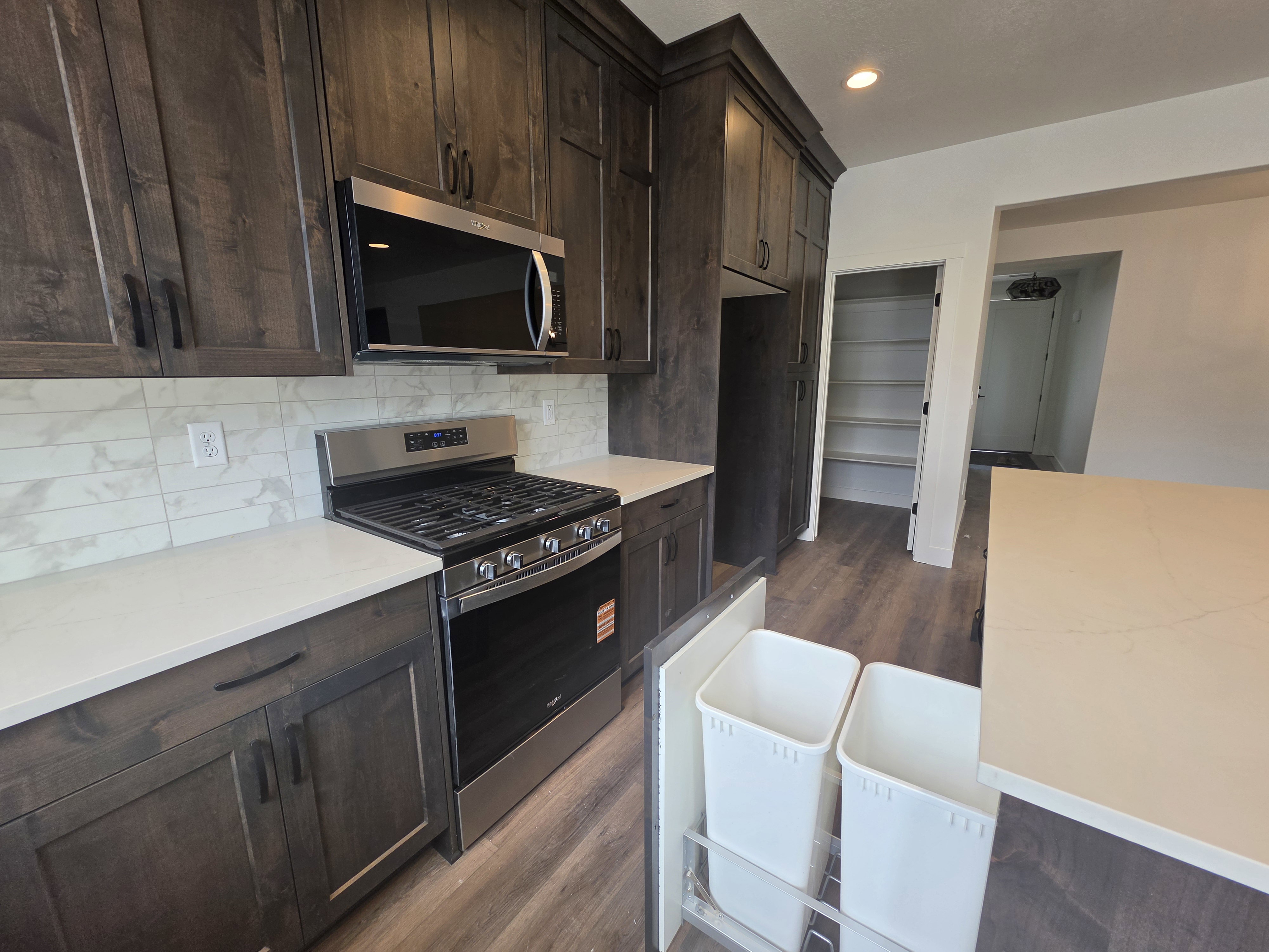 Modern kitchen featuring dark wood-finish cabinetry, stainless steel appliances, light-toned countertops, and a full-height tile backsplash