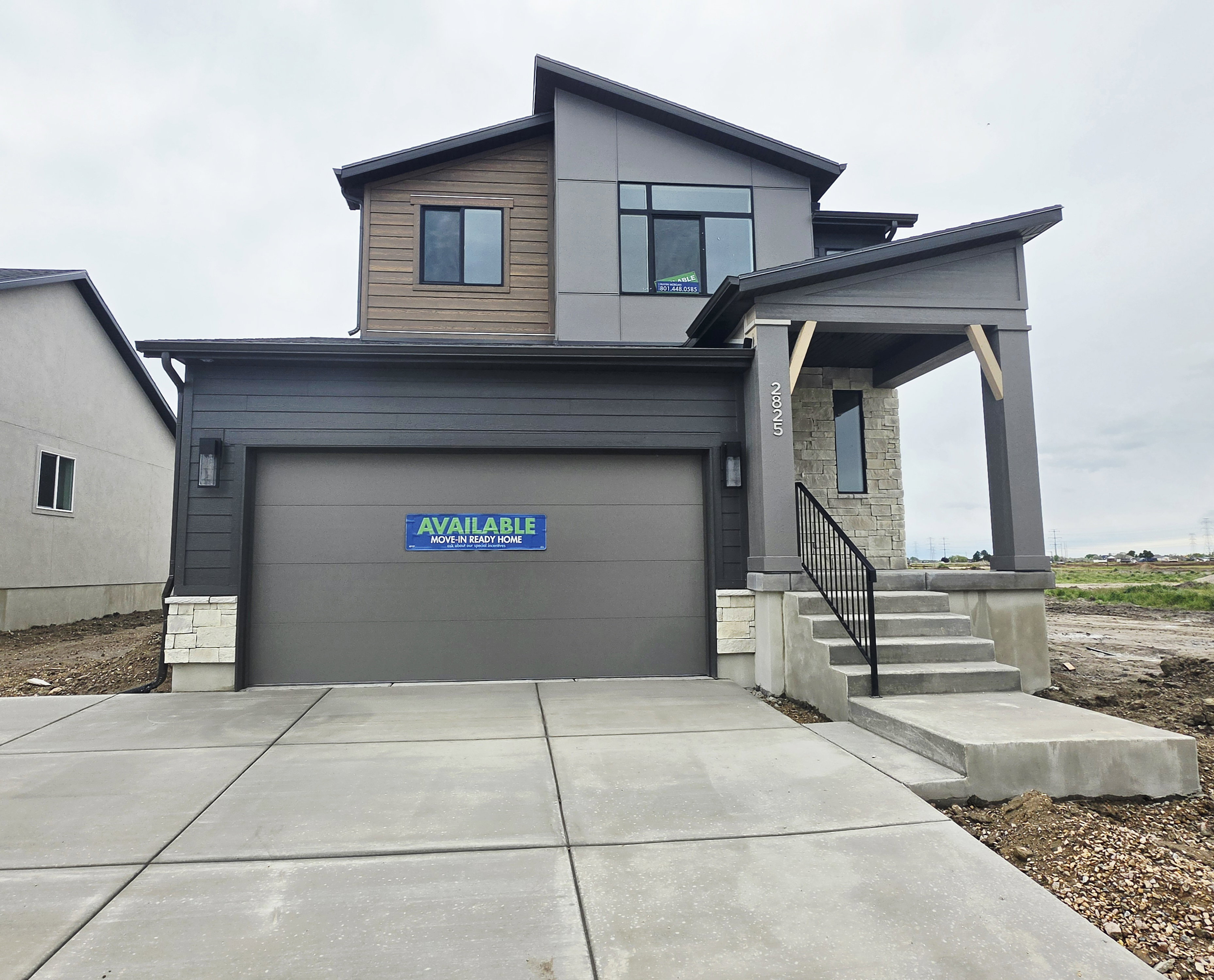 Contemporary two-story exterior featuring a multi-textured facade, an integrated garage, a covered entry with stone accents, a concrete driveway, and a front porch with an iron railing