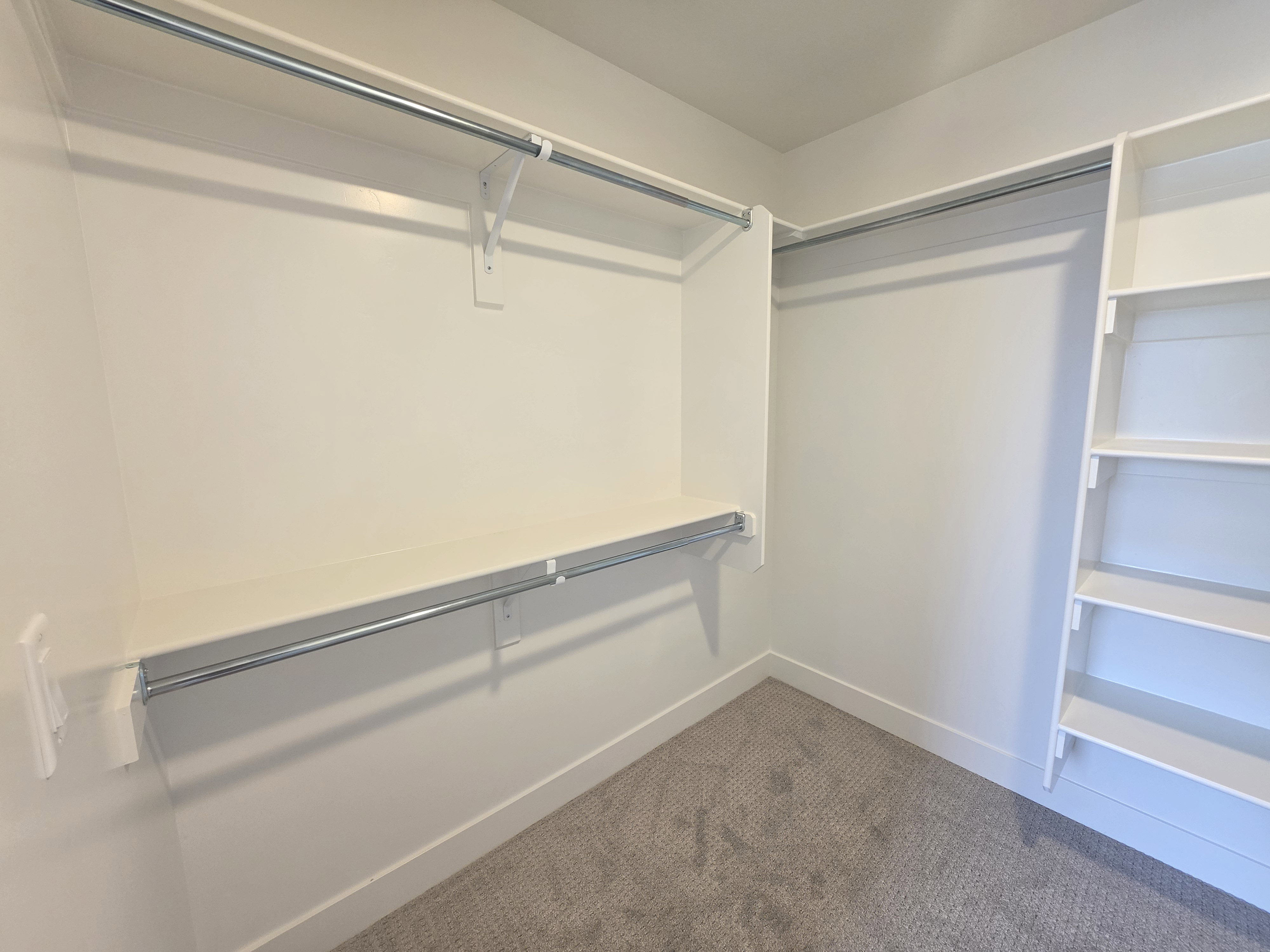 Walk-in closet with built-in shelving, hanging rods, and light gray carpeting