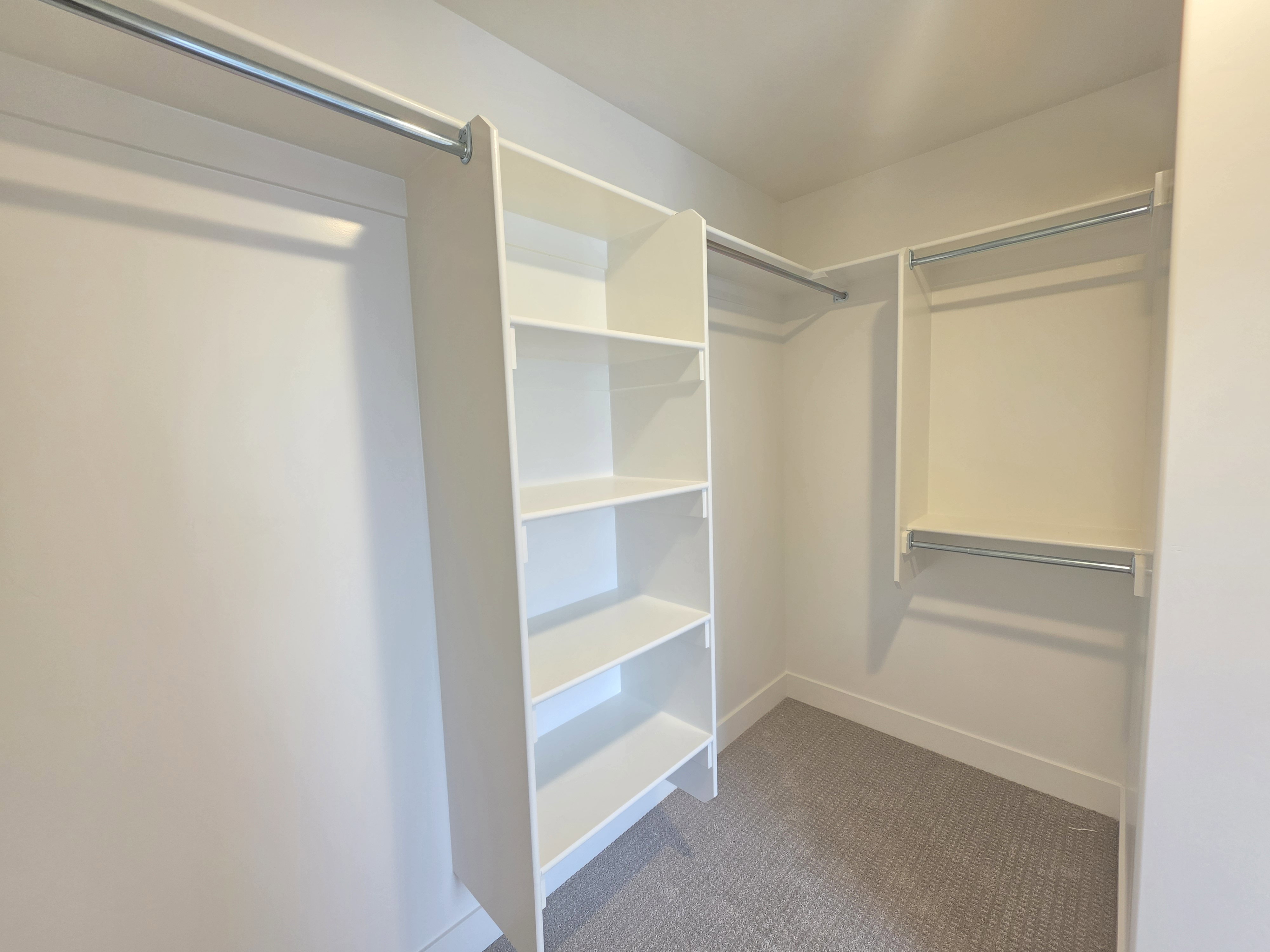 Custom closet system featuring built-in shelving, multiple hanging rods, white trim, and light gray carpet flooring