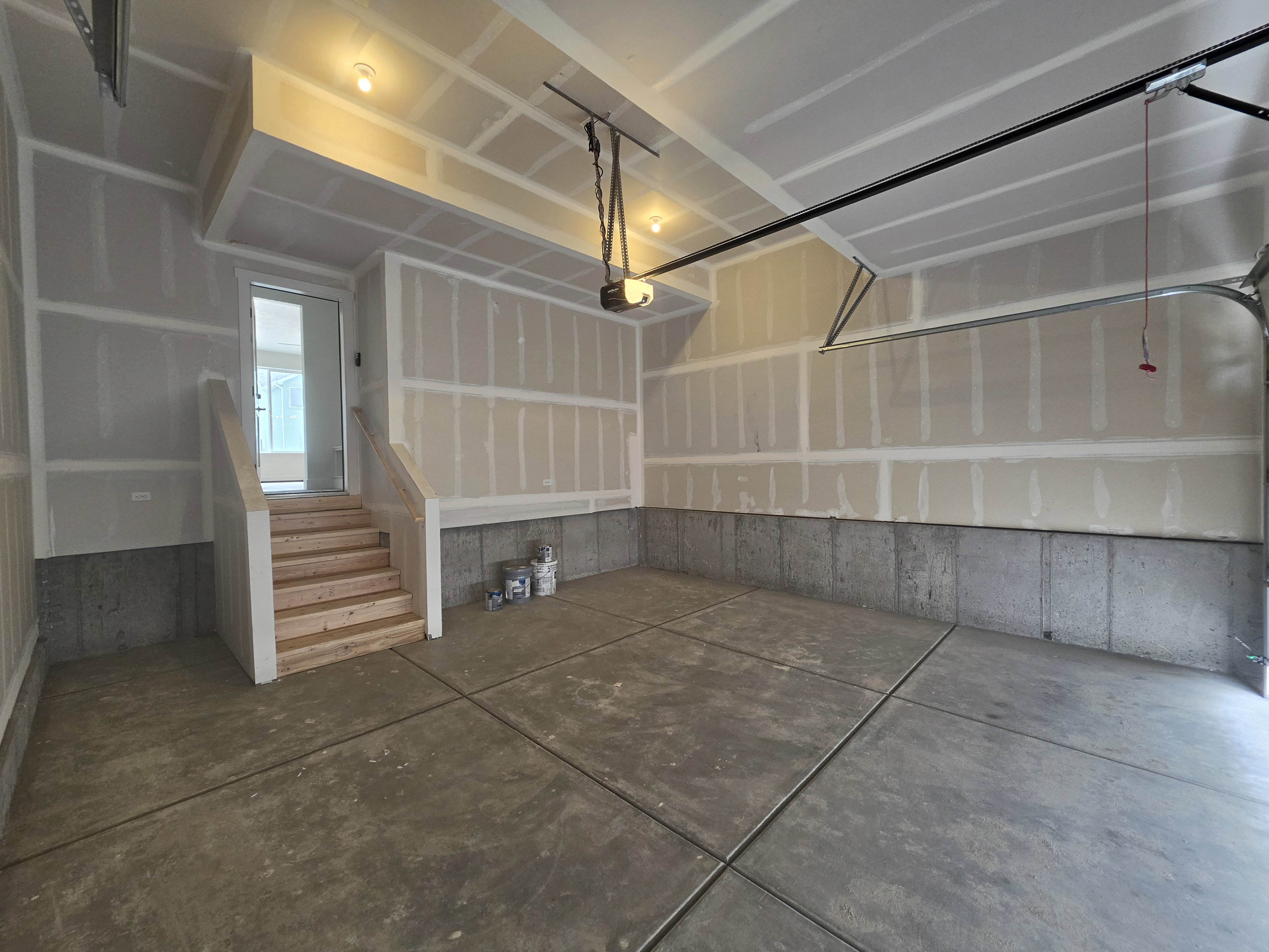 Spacious garage with a concrete floor, concrete wall paneling, and an interior staircase providing access to the property