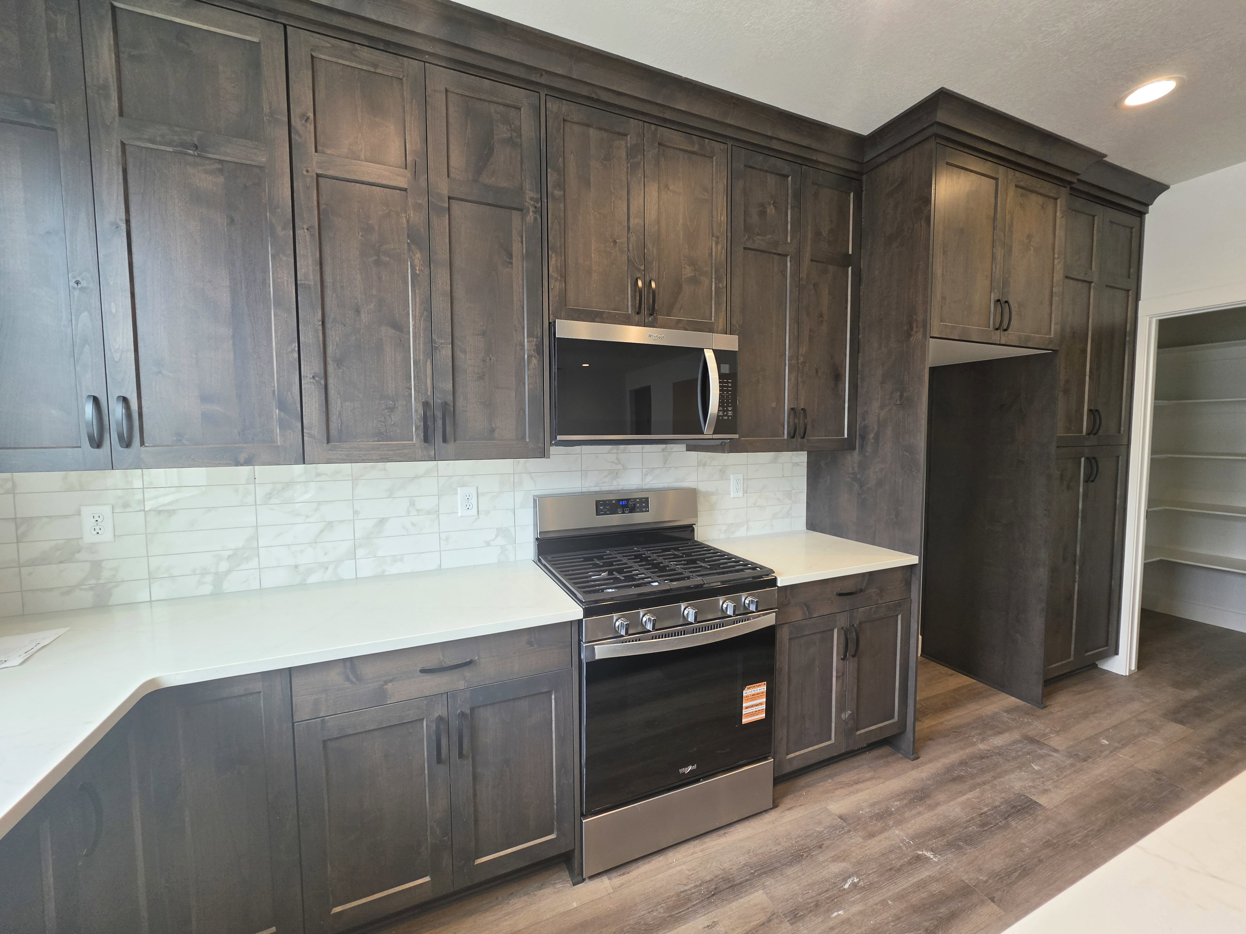 Kitchen featuring dark wood-finish cabinetry with crown molding, light-toned countertops, a subway tile backsplash, stainless steel appliances, and wood-look flooring