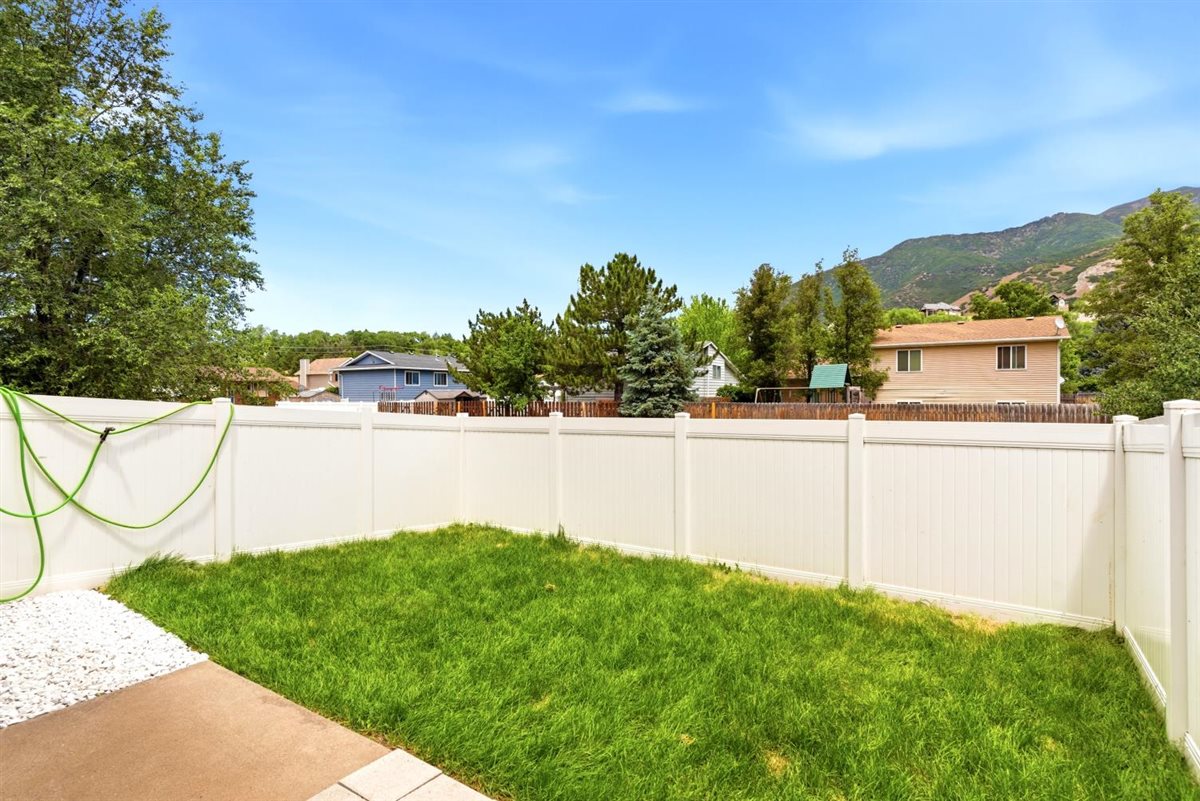 Expansive backyard featuring a lush lawn, white privacy fencing, and a concrete patio with white gravel accents