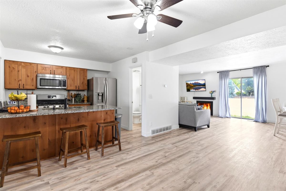 Open-concept living space featuring wood-finish flooring, a kitchen island with stone countertop, stainless steel appliances, and a living area with a fireplace