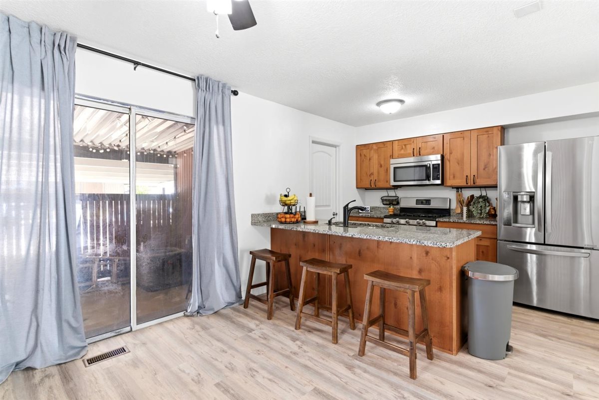 Kitchen featuring light wood-finish flooring, a central island with a granite-style countertop, light wood cabinetry, and stainless steel appliances