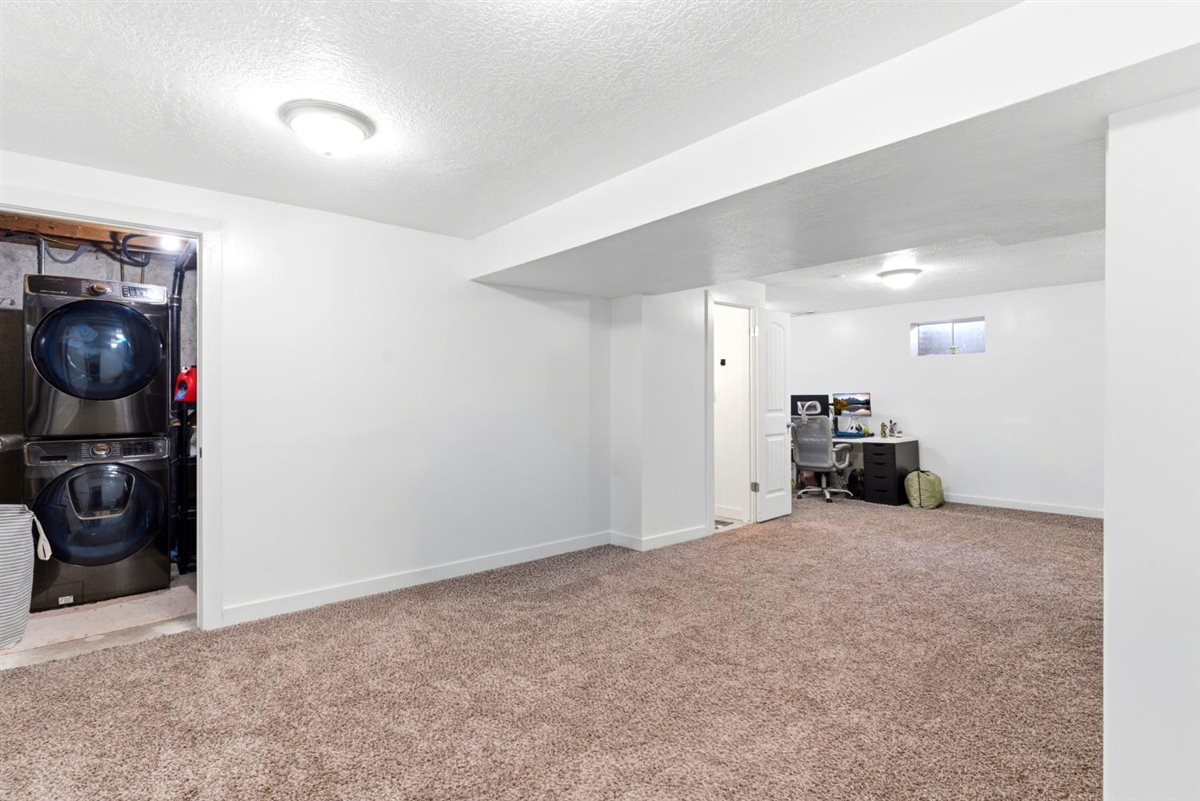 Spacious room featuring neutral carpeting, white walls, and a recessed laundry area with a stacked washer and dryer