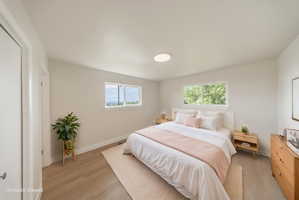 Bright bedroom featuring light wood-finish flooring and two windows with outdoor scenery