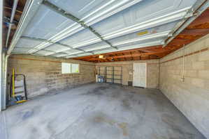 Spacious two-car garage featuring a concrete floor, exposed wood beam ceiling, and block wall construction
