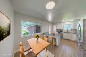 Contemporary kitchen featuring light wood-finish flooring, white cabinetry, stainless steel appliances, a light-toned countertop, and an eat-at island