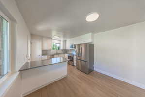 Contemporary kitchen featuring white cabinetry, stainless steel appliances, a breakfast bar with a solid surface countertop, and wood-finish flooring