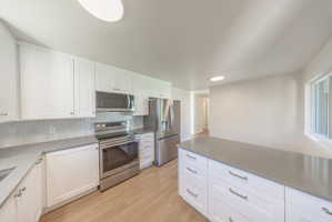 Modern kitchen featuring white cabinetry, stainless steel appliances, a light gray countertop, a subway tile backsplash, and wood-finish flooring