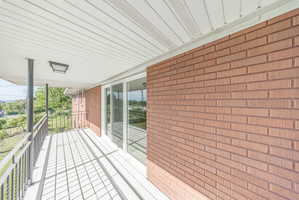 Covered balcony featuring red brick siding, white vinyl soffit, black metal railing, and sliding glass doors