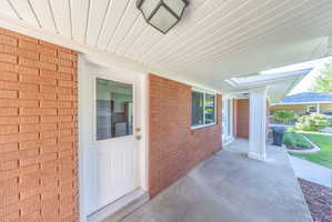 Covered concrete porch with a white paneled soffit, brick facade, white framed windows, and a white entry door