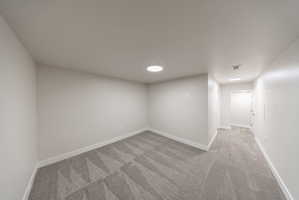 Spacious room featuring light gray patterned carpeting, white baseboards, and a circular ceiling light