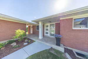Brick exterior featuring a modern front door with frosted glass panels, a covered porch entry, white pillar, and clean landscaping with mature plantings