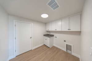 Dedicated utility area featuring wood-finish flooring, white cabinetry, a built-in sink with a dark countertop, and laundry hookups