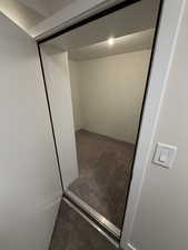 Carpeted interior space featuring a recessed ceiling light, textured concrete walls, and a white rocker light switch