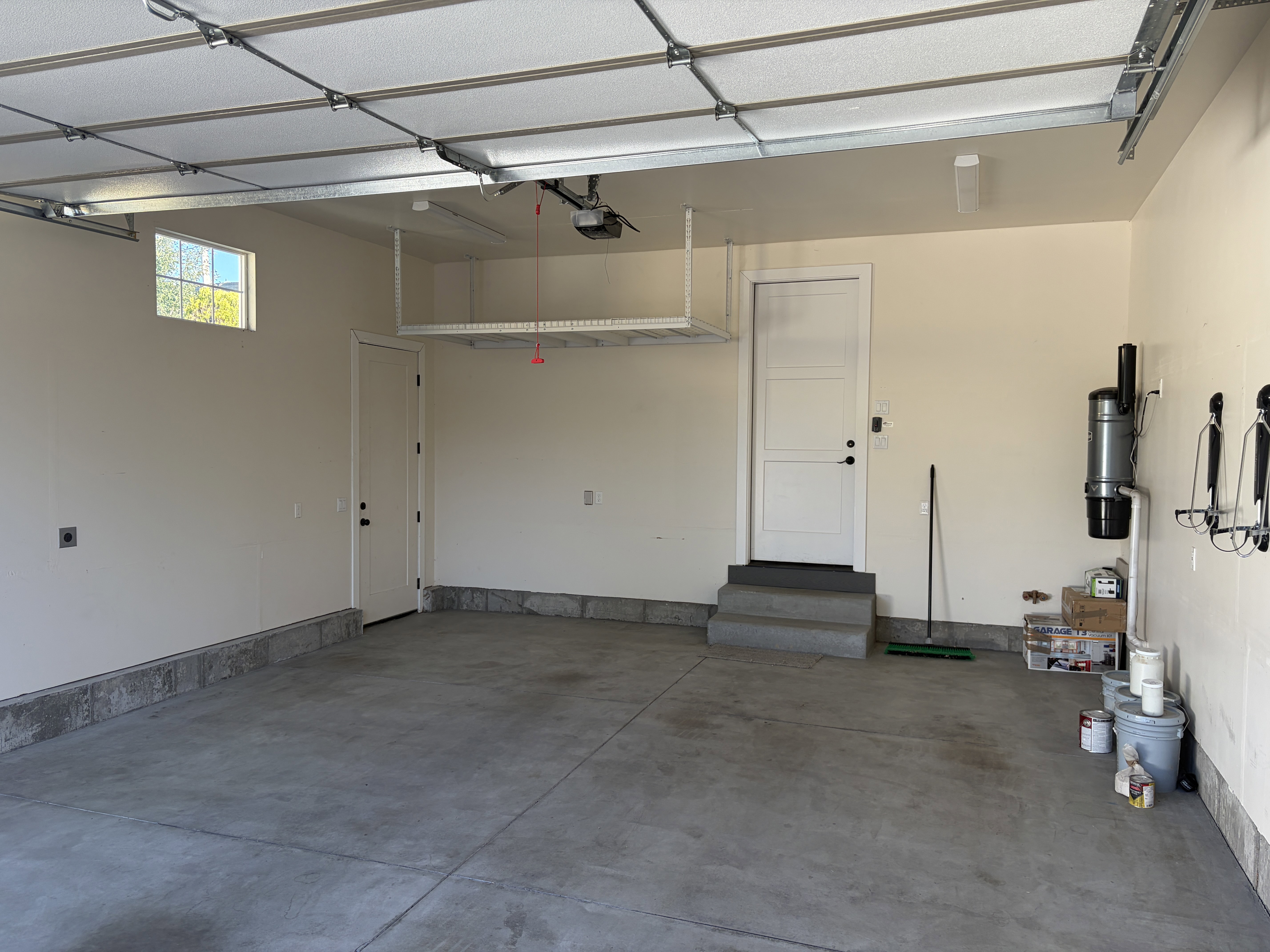 Spacious garage featuring a concrete floor, overhead storage rack, transom window, and a central vacuum system