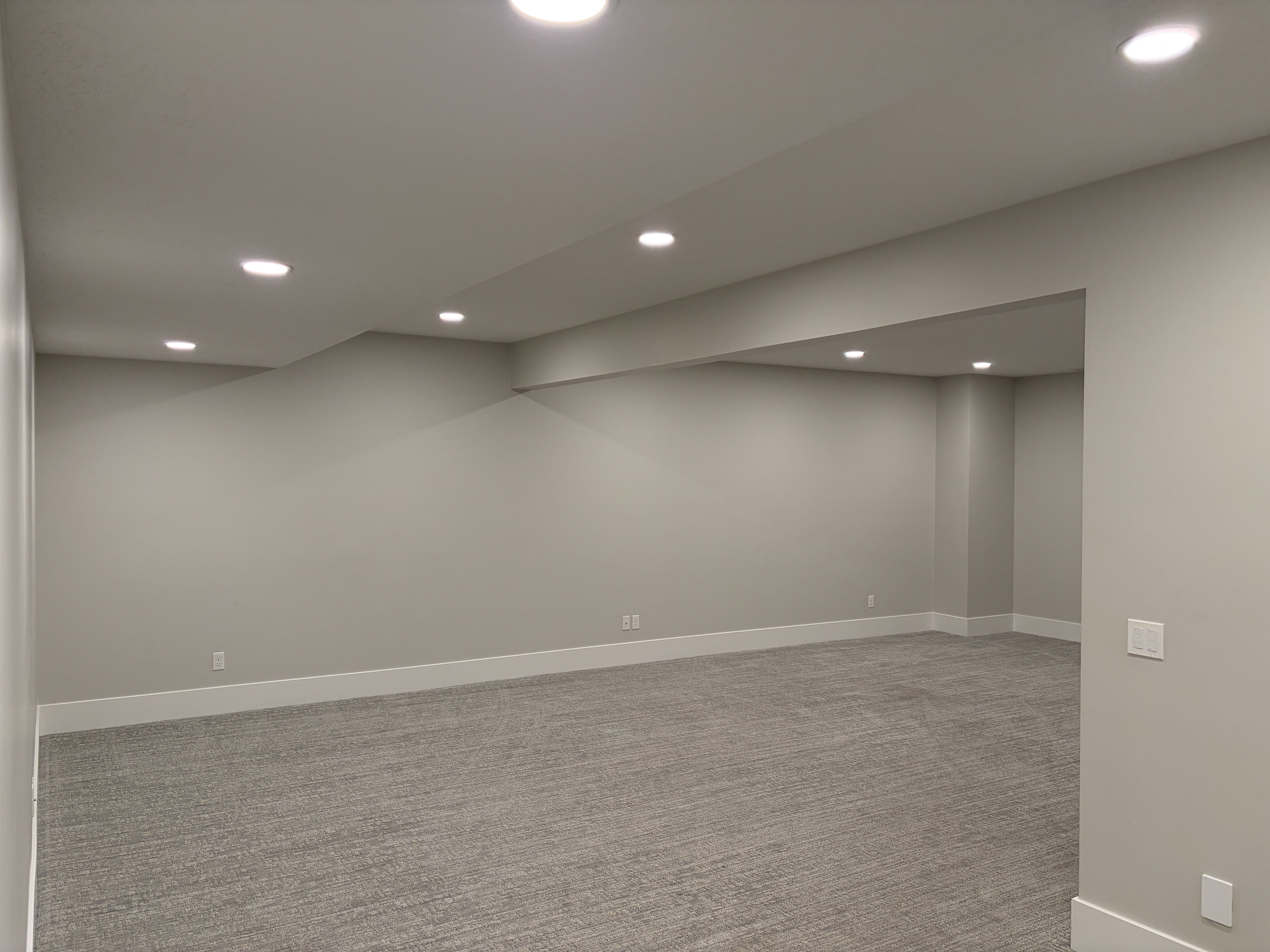 Spacious room featuring neutral carpeting, recessed ceiling lighting, light gray walls, white baseboards, and an open entryway