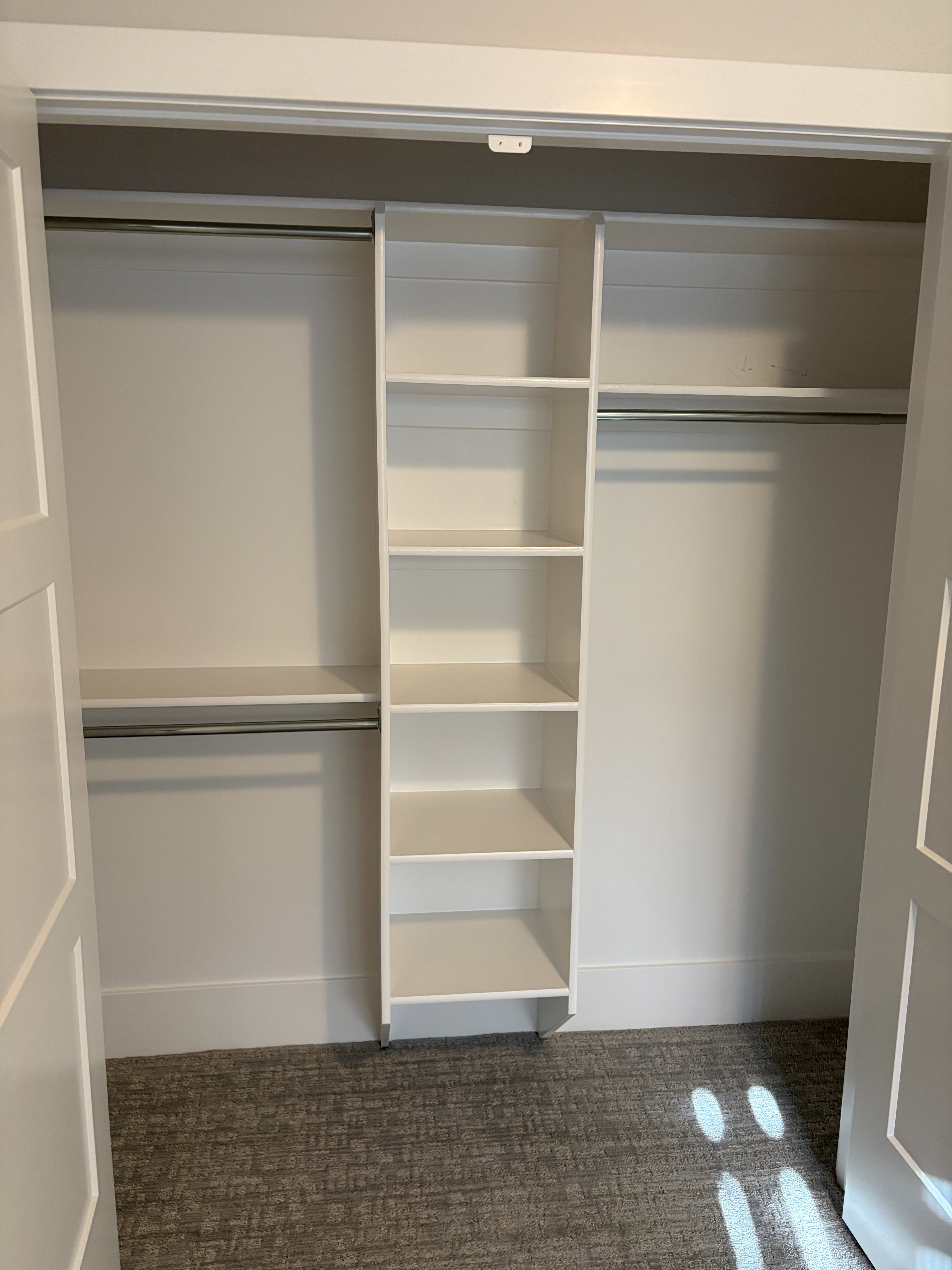 Bifold closet doors reveal a custom closet system featuring white built-in shelving, dual hanging rods, and an upper storage shelf