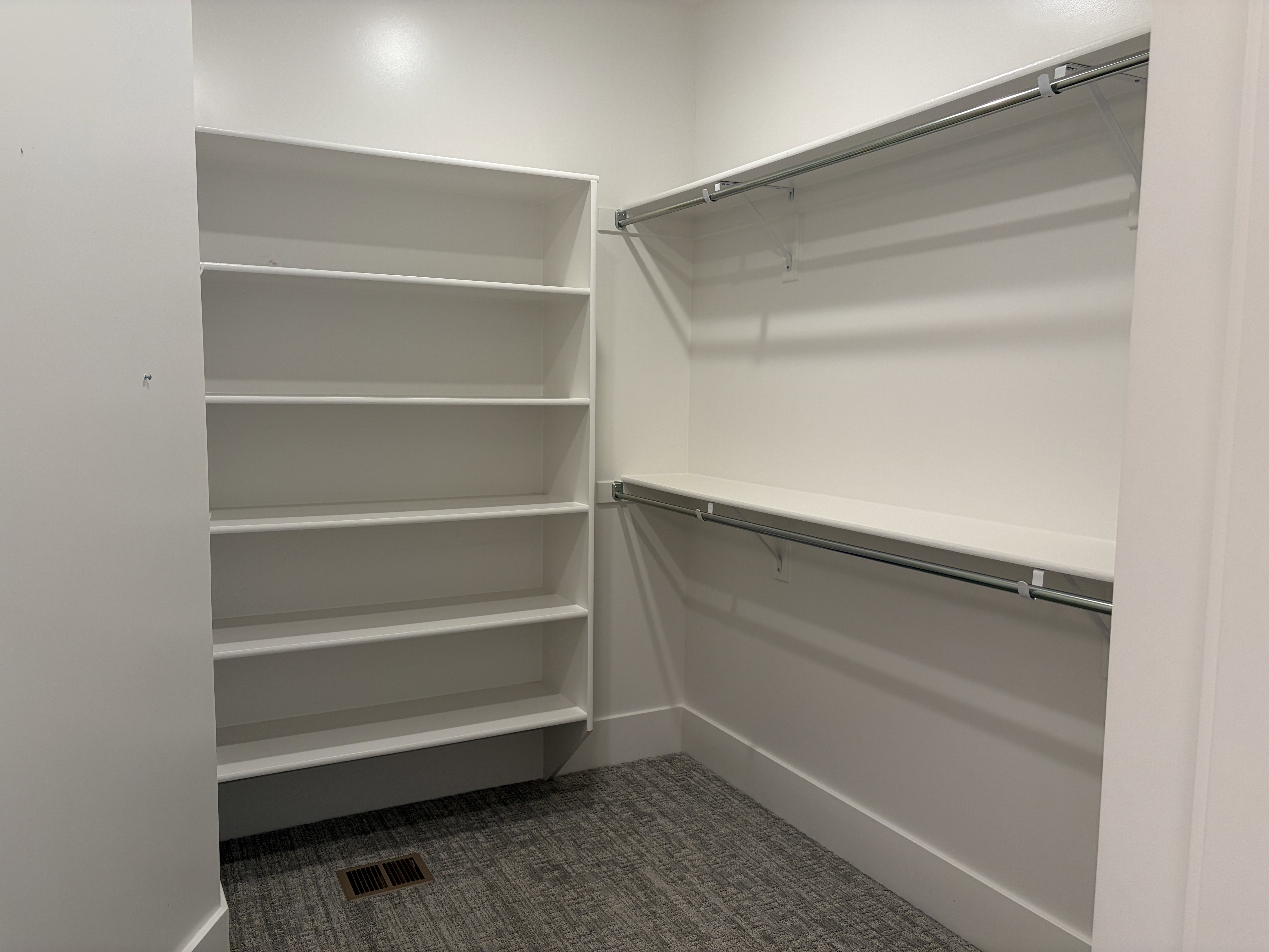 Walk-in closet featuring white built-in shelving, dual hanging rods, and gray patterned carpet