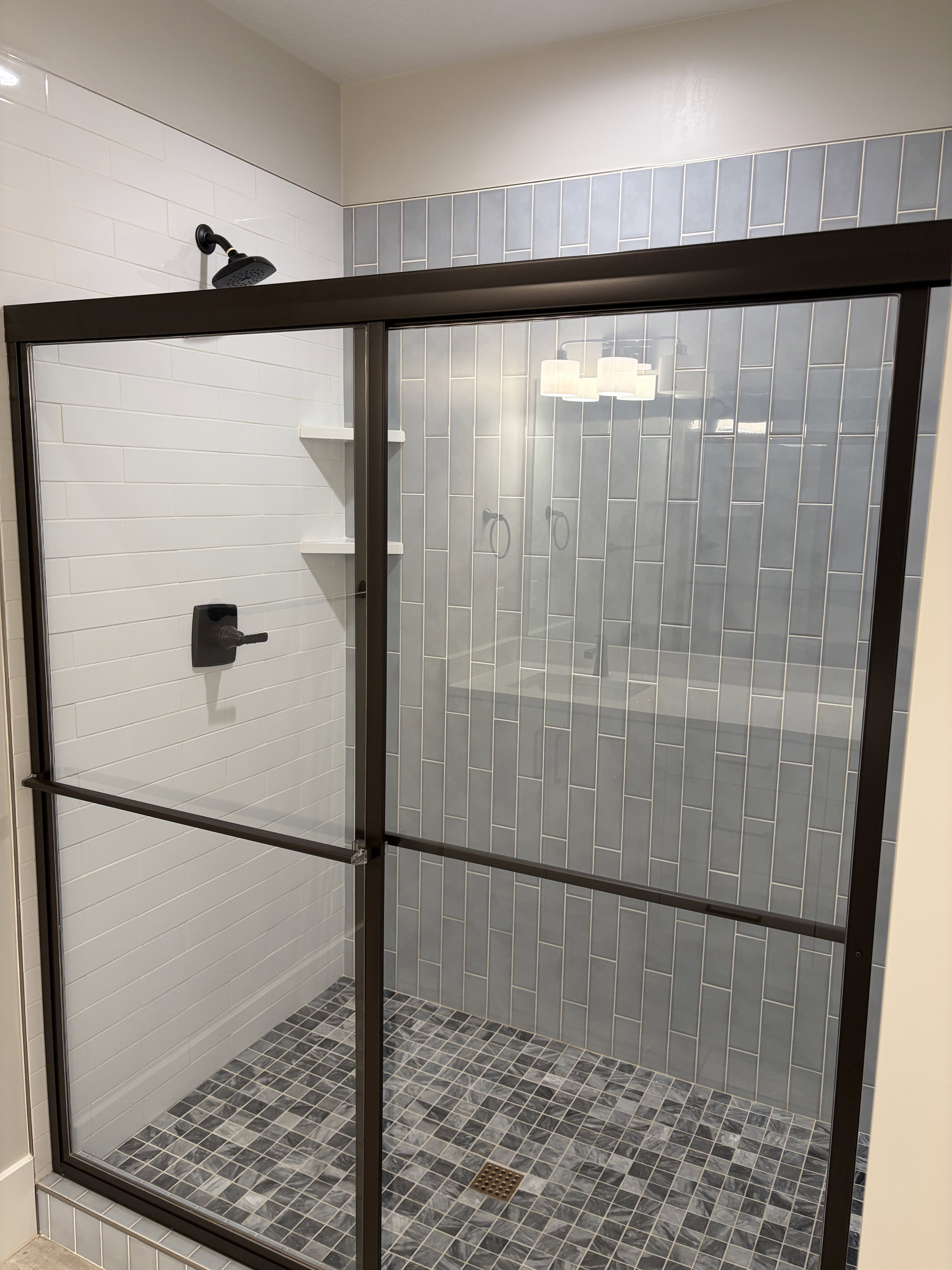 Walk-in shower featuring a dark bronze framed glass enclosure, matte black shower fixtures, mosaic tile flooring, and integrated wall shelving