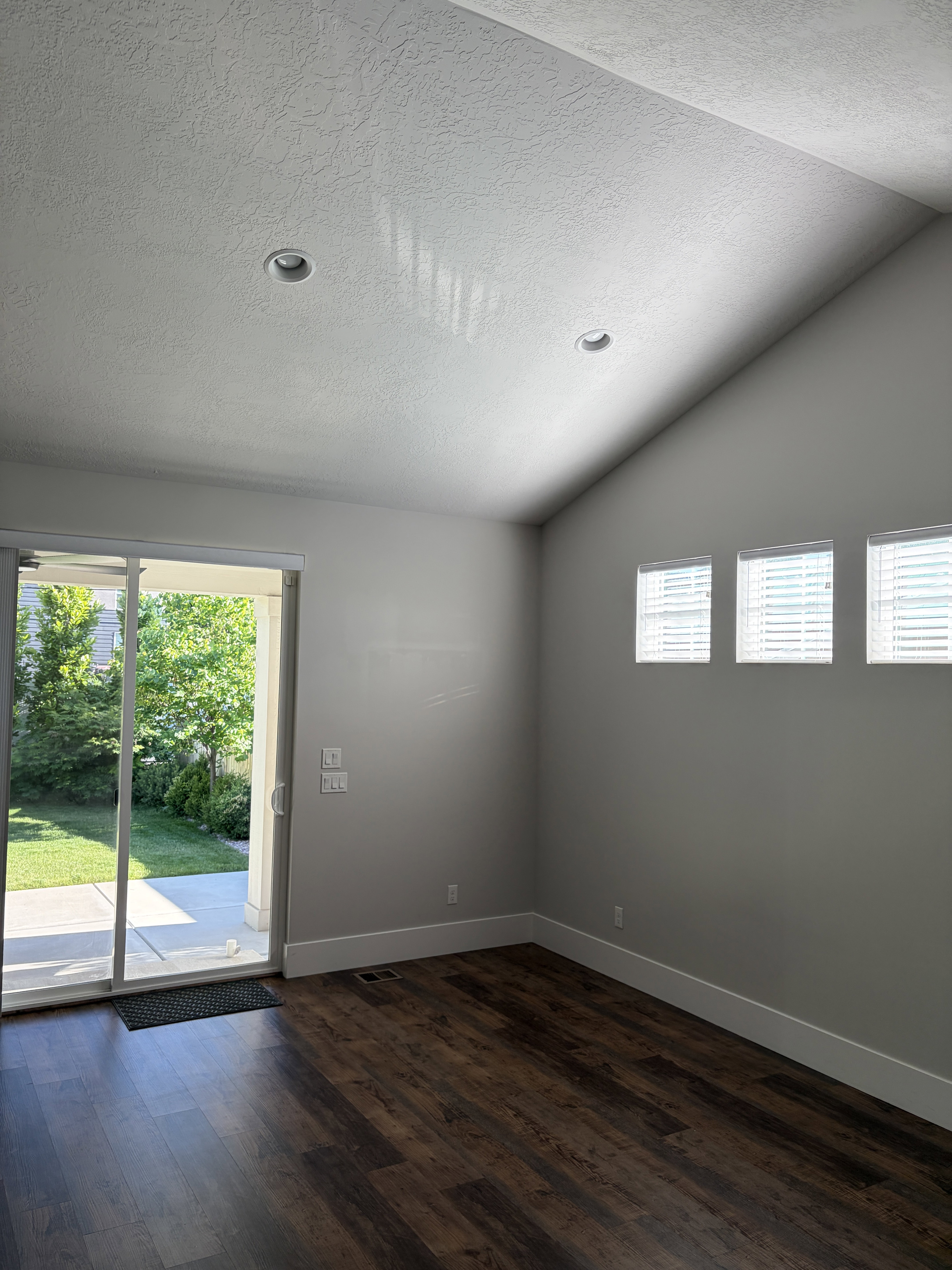 Vaulted ceiling with recessed lighting, wood-finish flooring, sliding glass patio door, three rectangular windows, and white baseboards